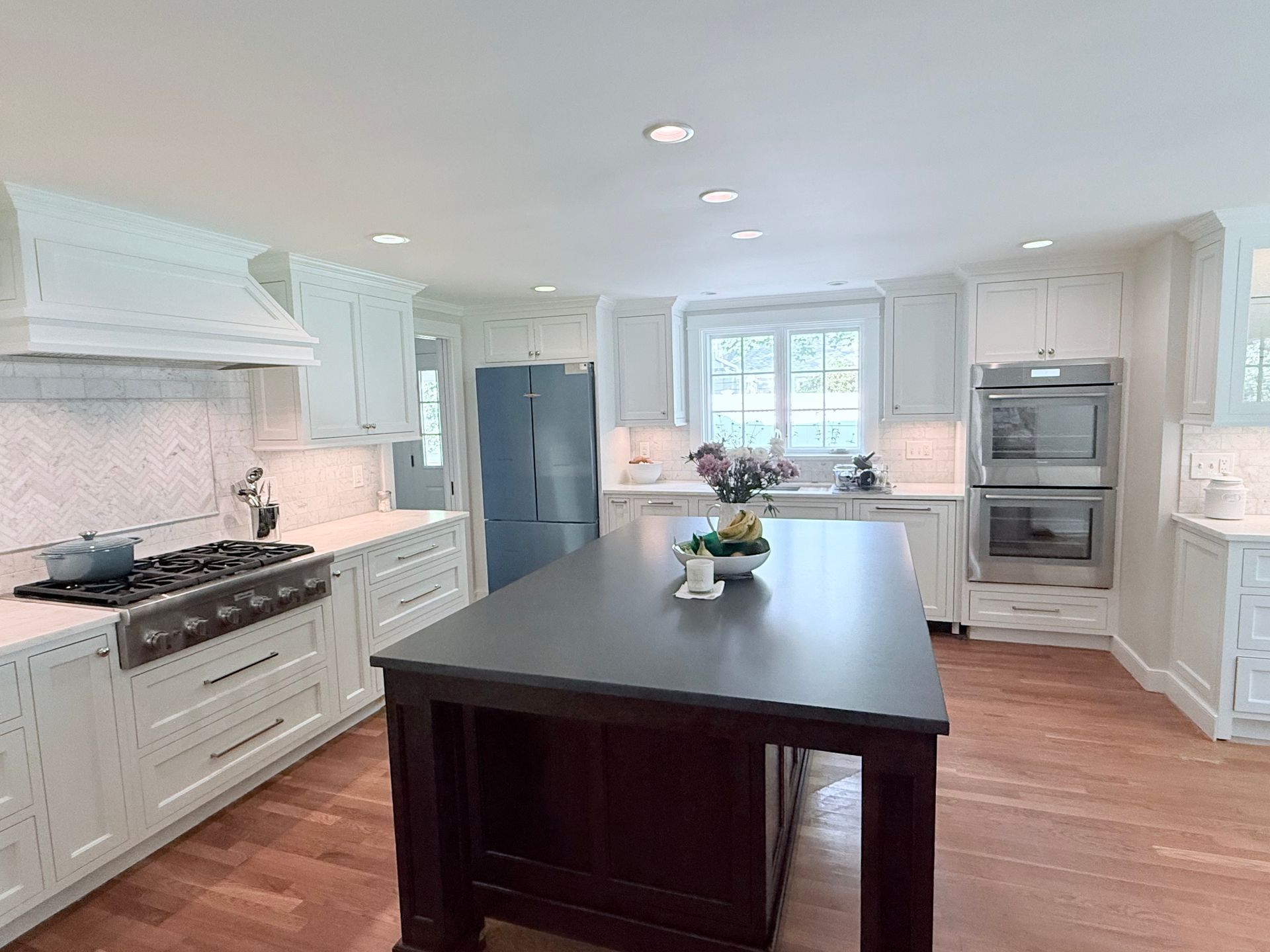 Bright white kitchen with a large dark island, stainless steel appliances, and hardwood floors.