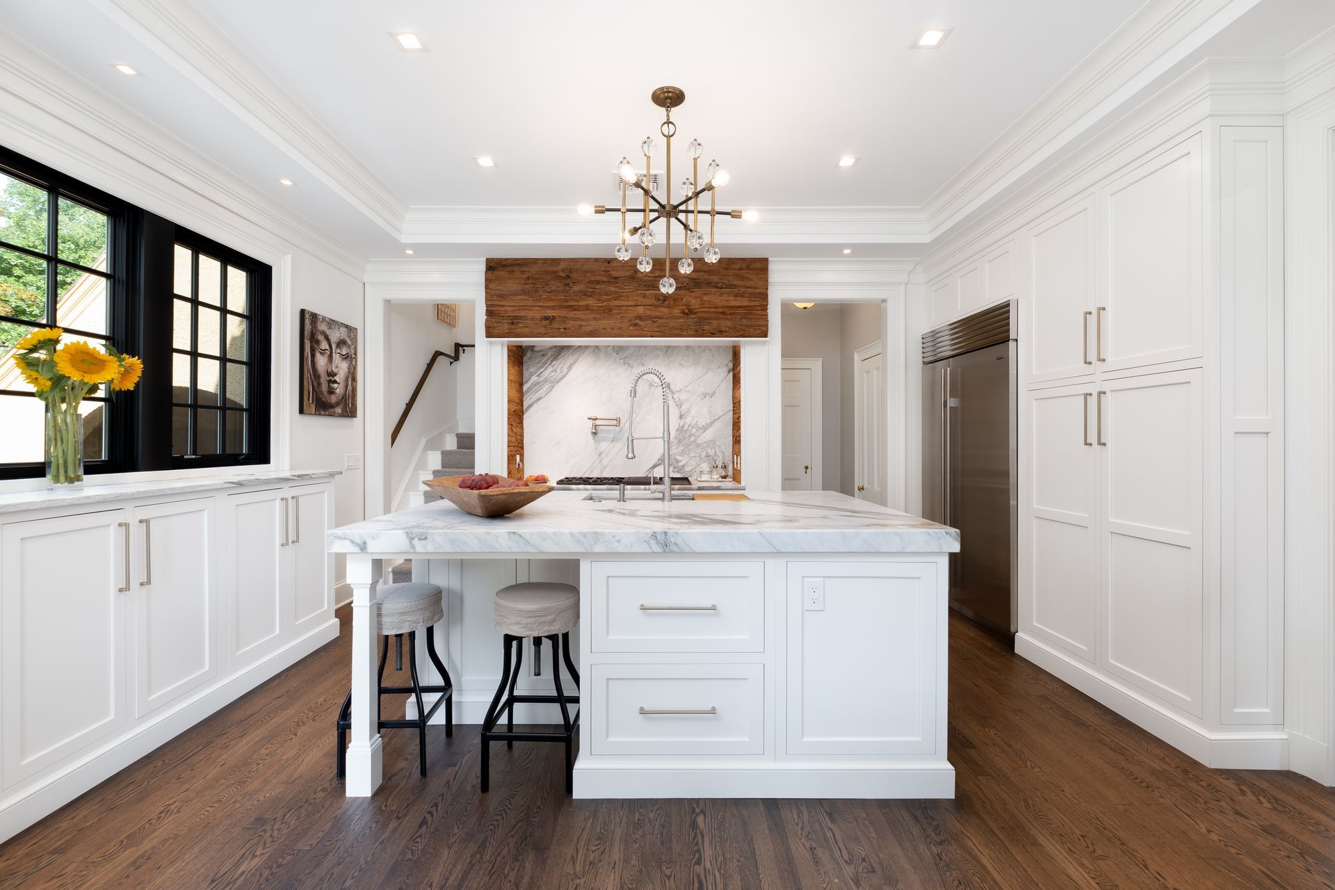 Bright white modern kitchen with marble island, dark wood floor, black windows, and copper range hood