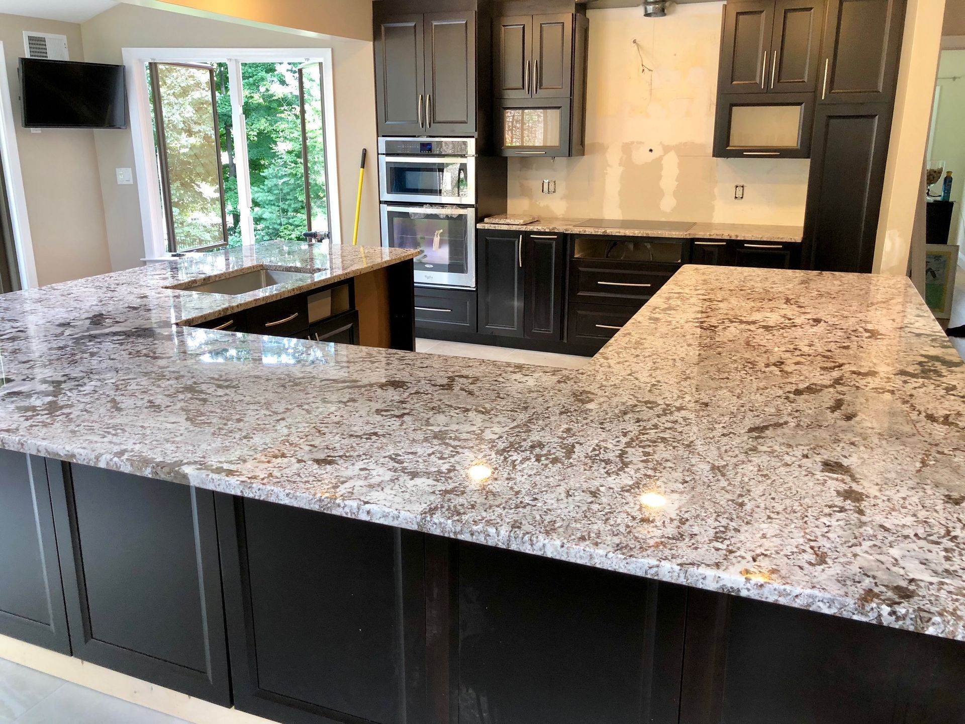 Modern kitchen with granite island, dark cabinets, stainless appliances, and sliding glass doors.