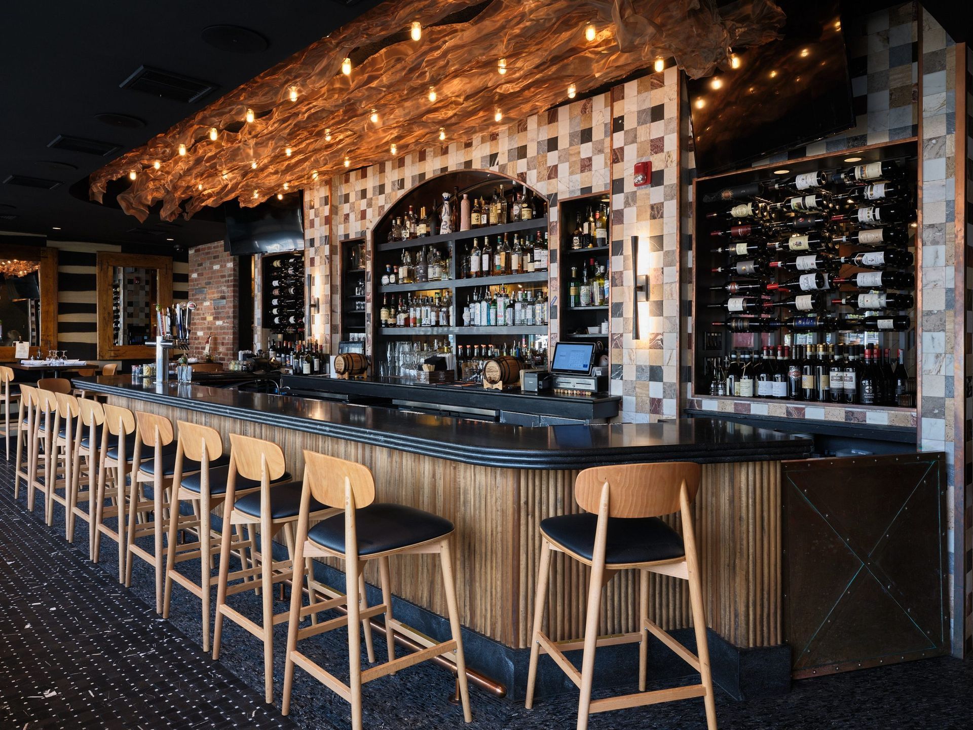 Stylish bar interior with wooden stools, patterned tile walls, and shelves of bottles behind the counter
