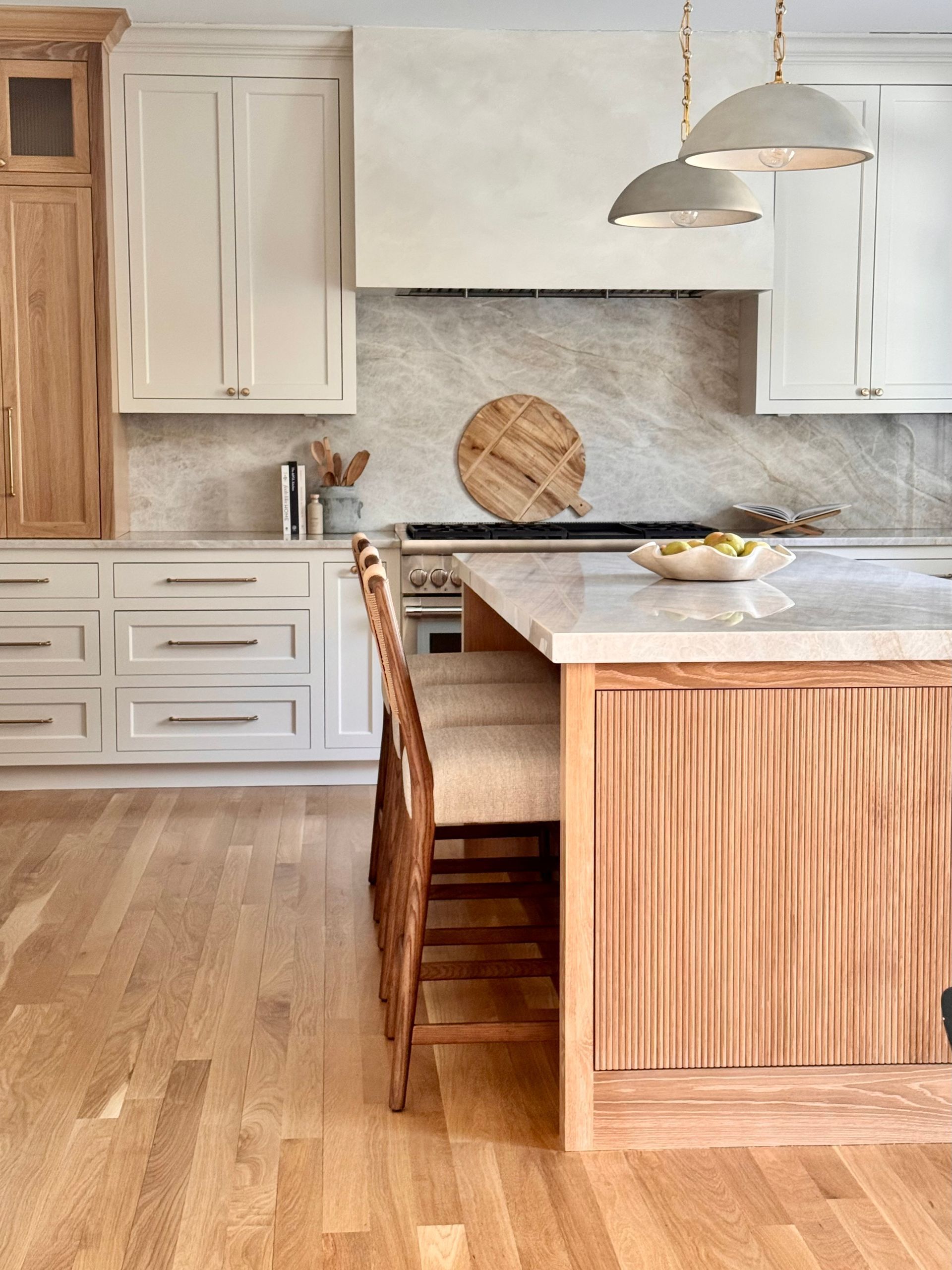 Modern kitchen with white cabinets, wood accents, marble island, and pendant lights