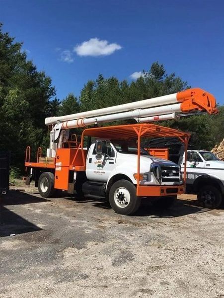 An orange and white bucket truck parked on a gravel lot under a bright blue, sunny sky with trees in the background.