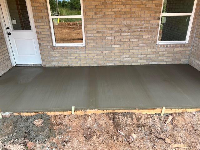 Newly poured concrete patio outside a brick building, with door and windows visible.