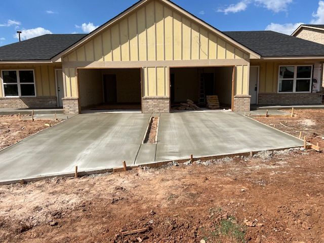 New concrete driveway in front of two-car garage under construction, adjacent to a home with yellow siding.