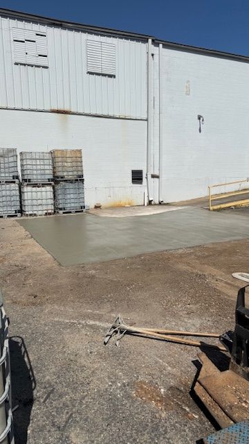 A newly poured concrete pad in front of a white industrial building.