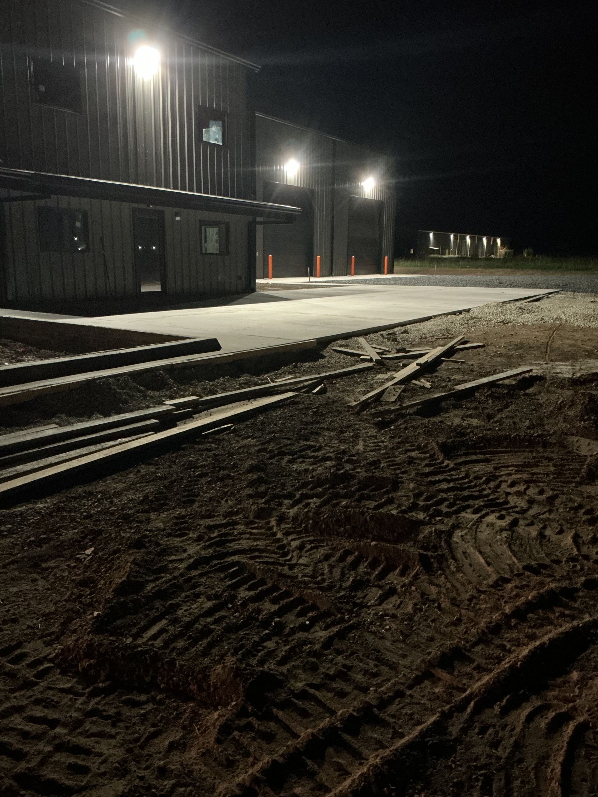 A dimly lit industrial building at night, with bright overhead lights illuminating the structure and surrounding ground.