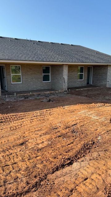 New construction townhomes with gray shingle roofs, beige brick exterior, and windows in a dirt lot.