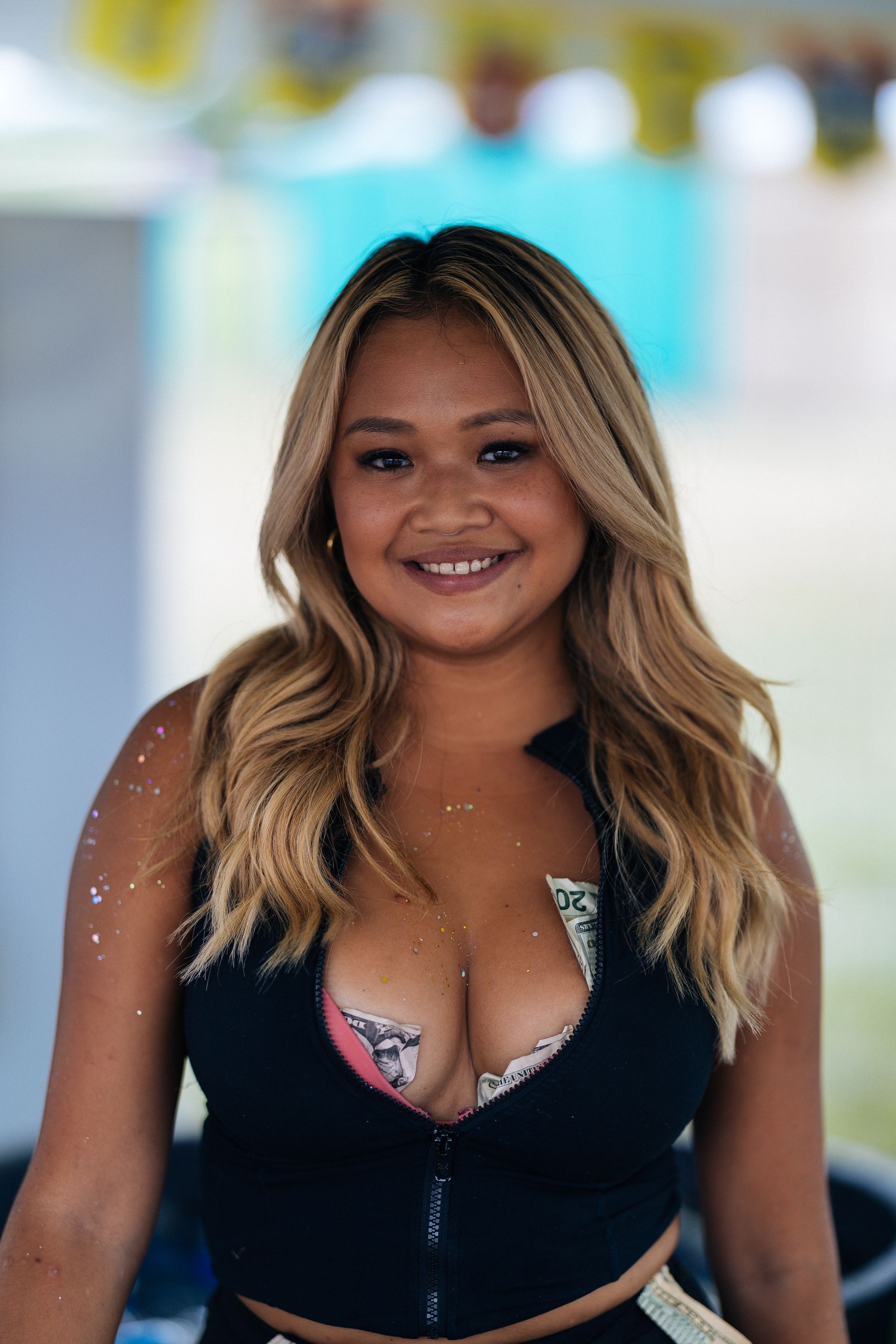 Smiling woman with blonde hair, money tucked into her top. Outdoors, light skin.