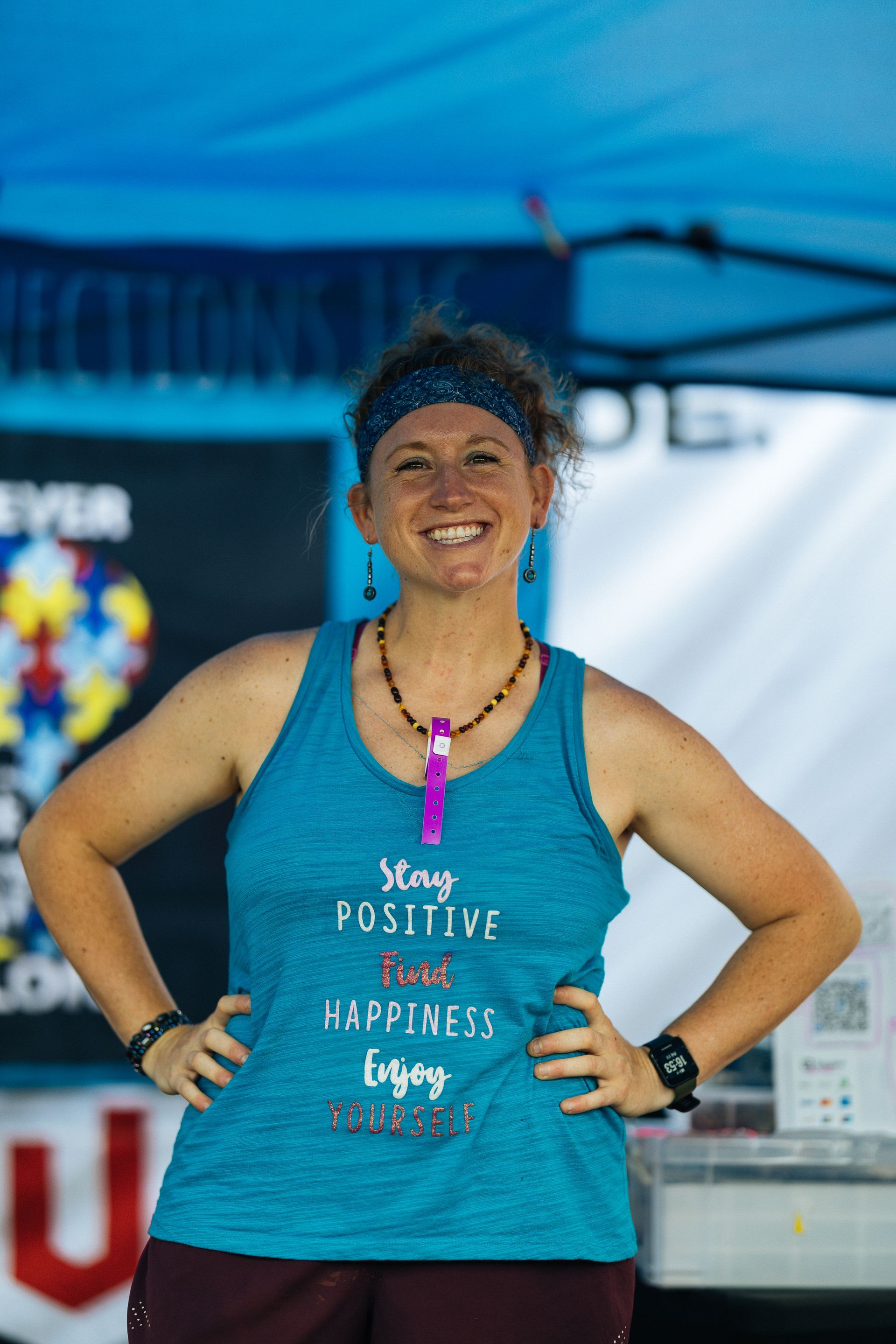 Woman wearing a teal tank top with “Stay Positive” text, smiling with hands on hips.
