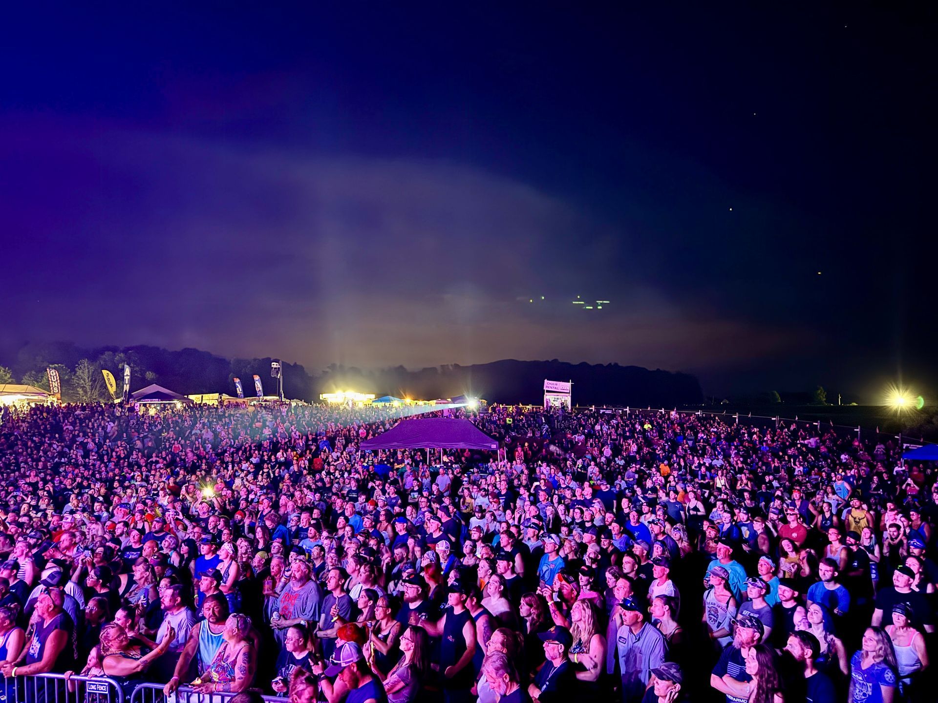 Large crowd at an outdoor concert at night under blue and purple lights.
