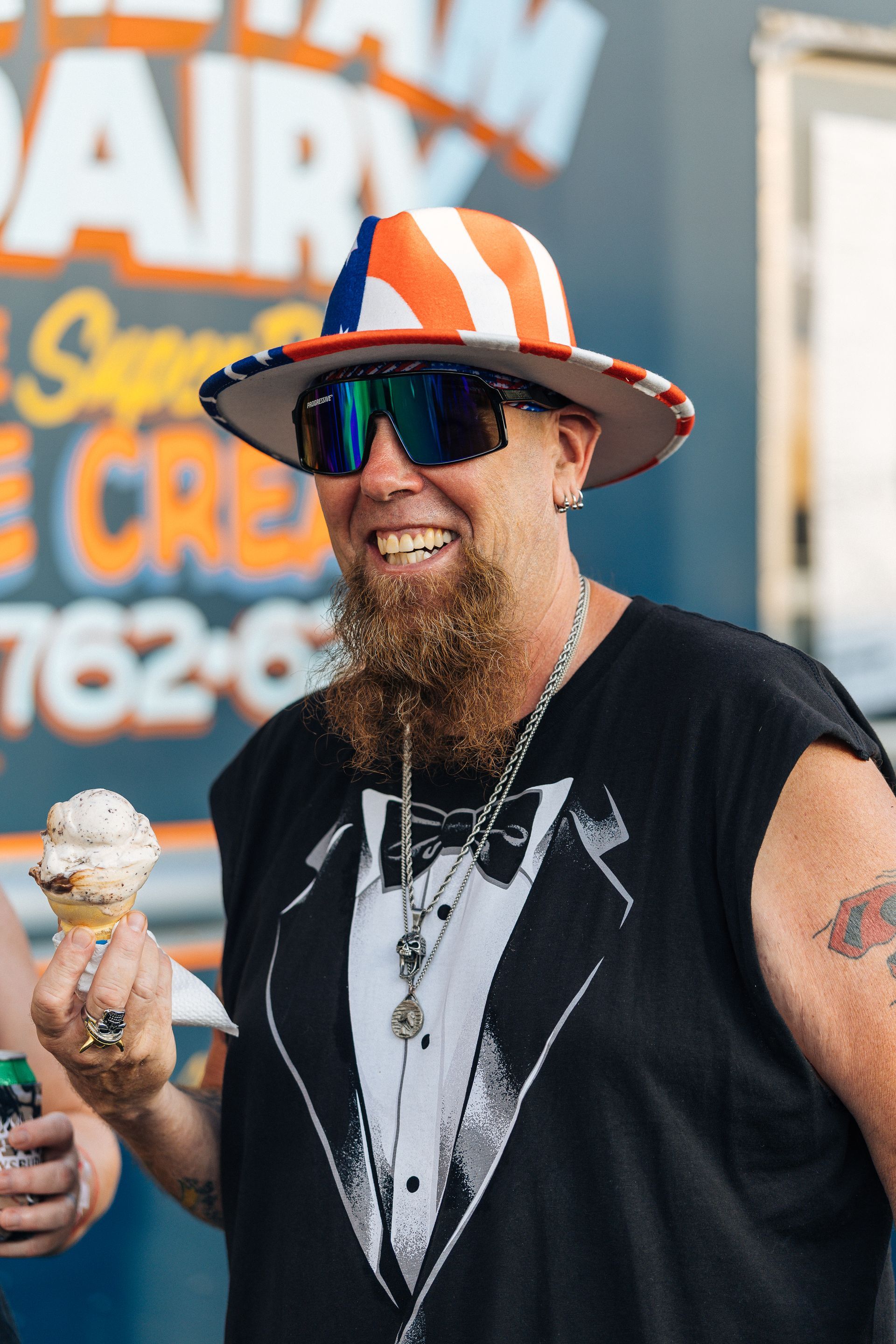 Man in patriotic hat and sunglasses smiles while holding ice cream cone.