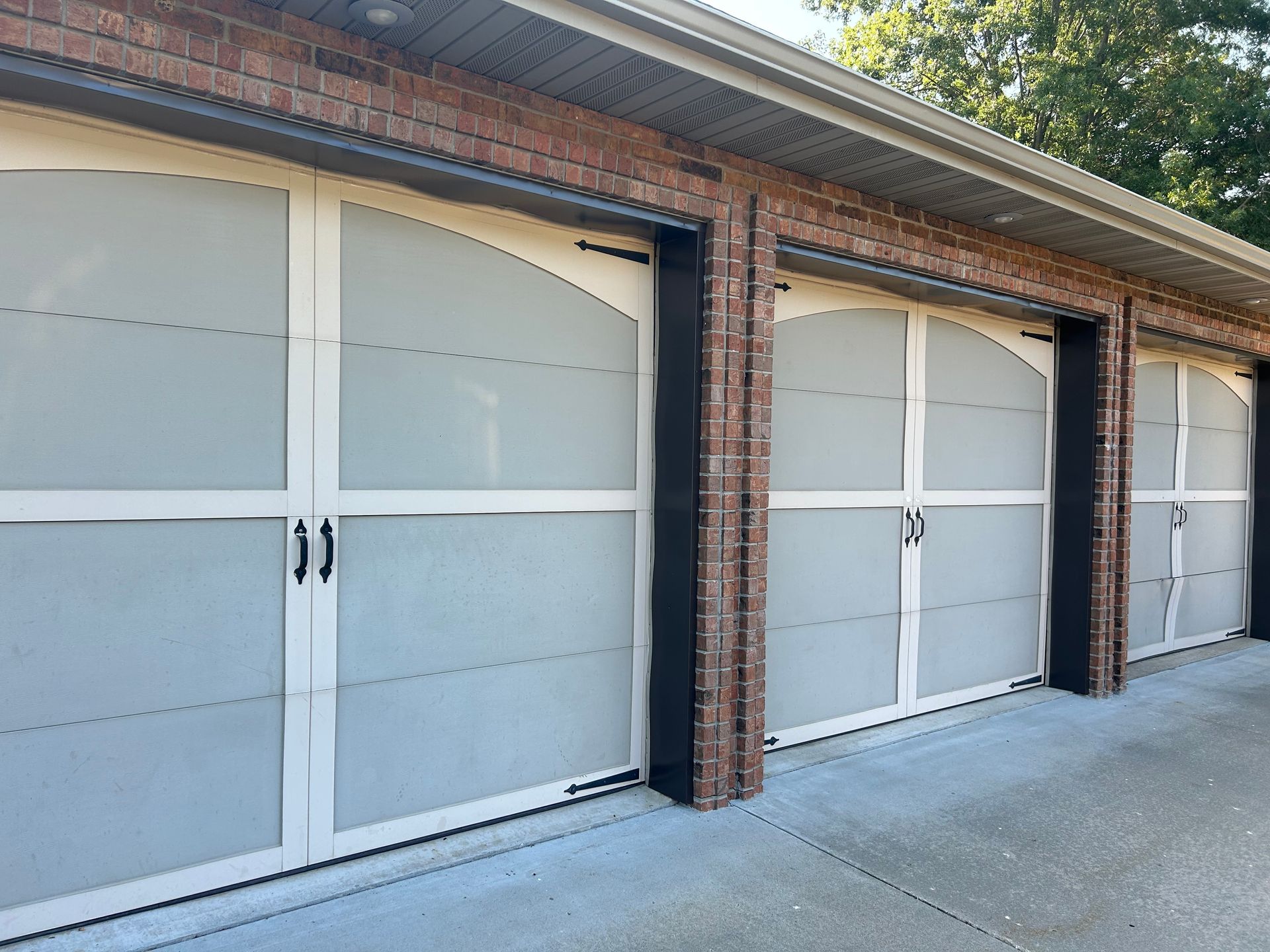 Three white and grey garage doors with black accents set in a brick exterior.