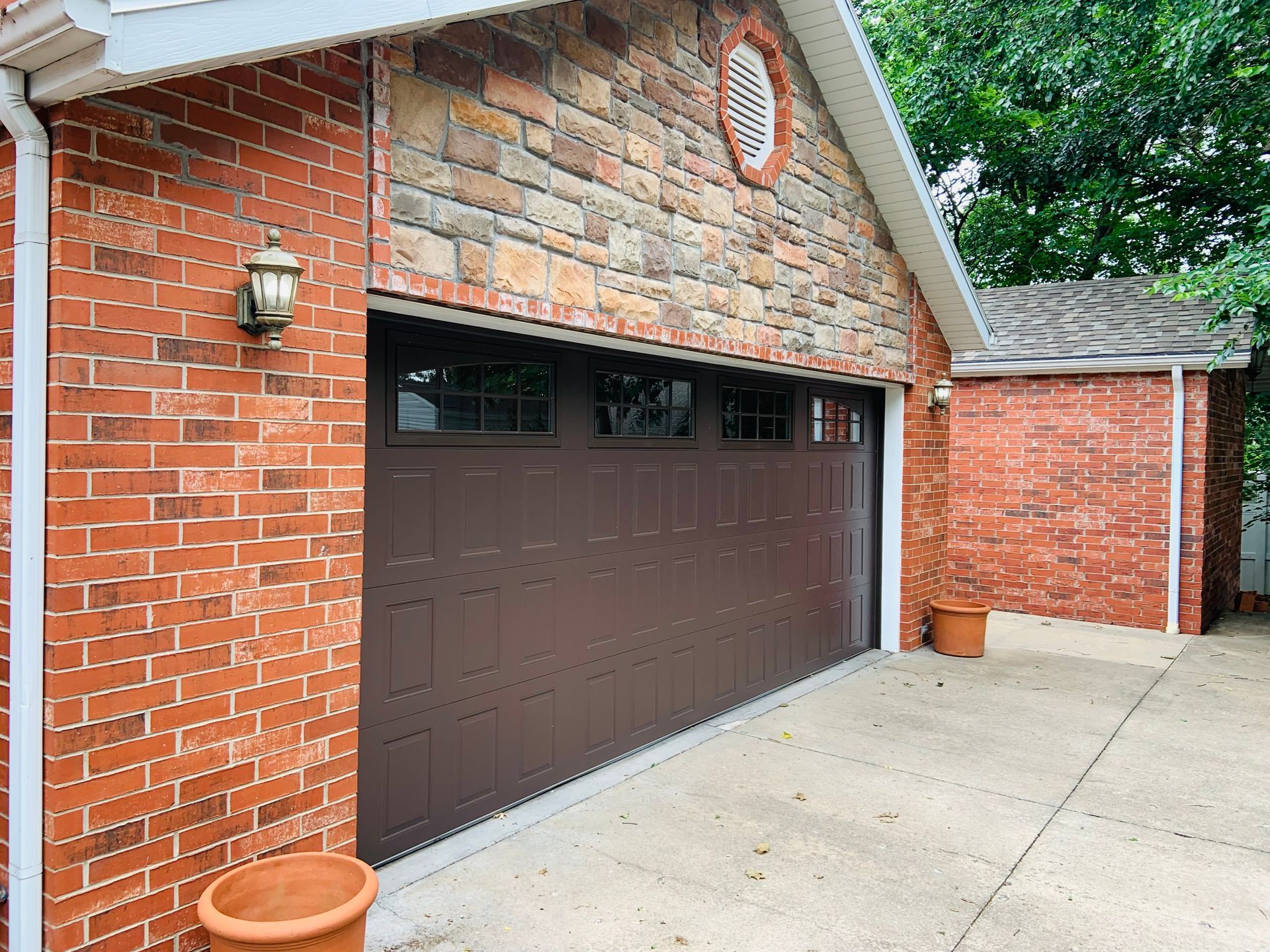 Brown garage door on a brick building with stone above. Small brick building to the right.