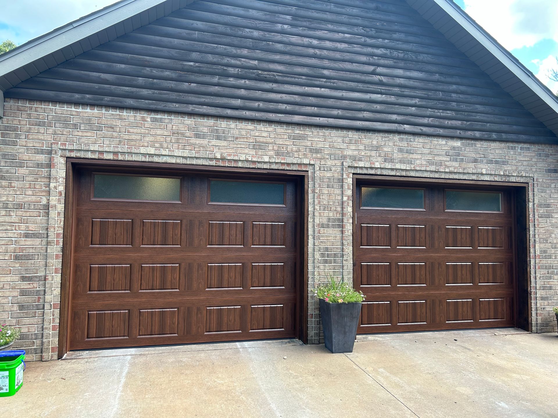 Brown garage doors on a brick house; plant in a tall, dark planter.