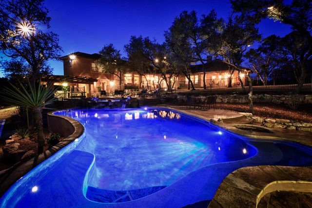 A large swimming pool is lit up at night in front of a large house