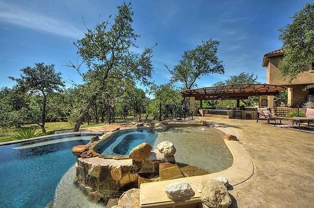 A large swimming pool is surrounded by rocks and trees in front of a house