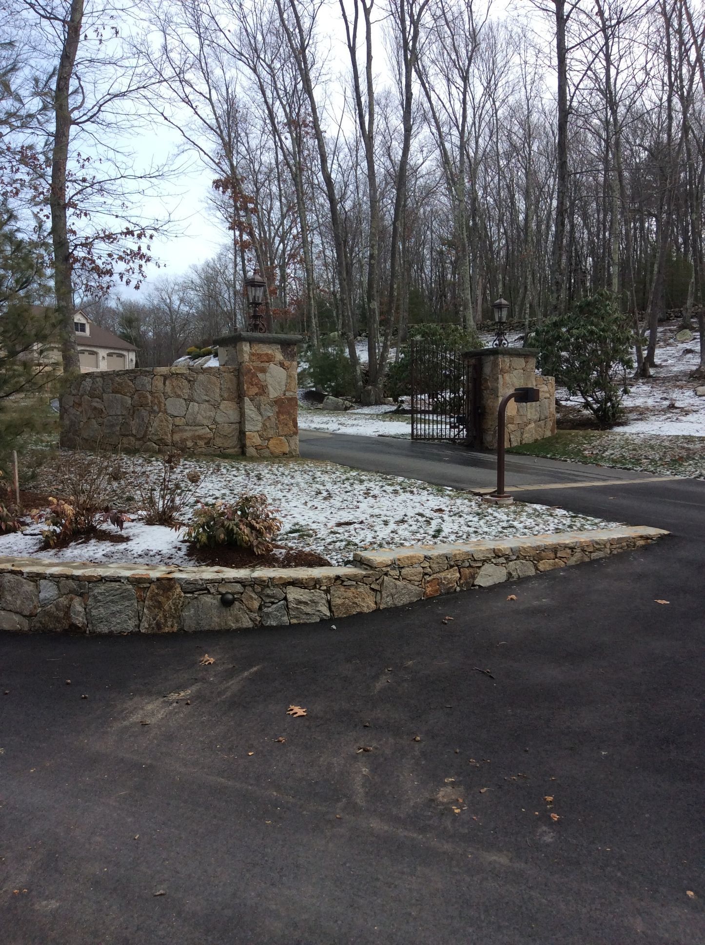 a stone wall surrounds a driveway leading to a house in the woods
