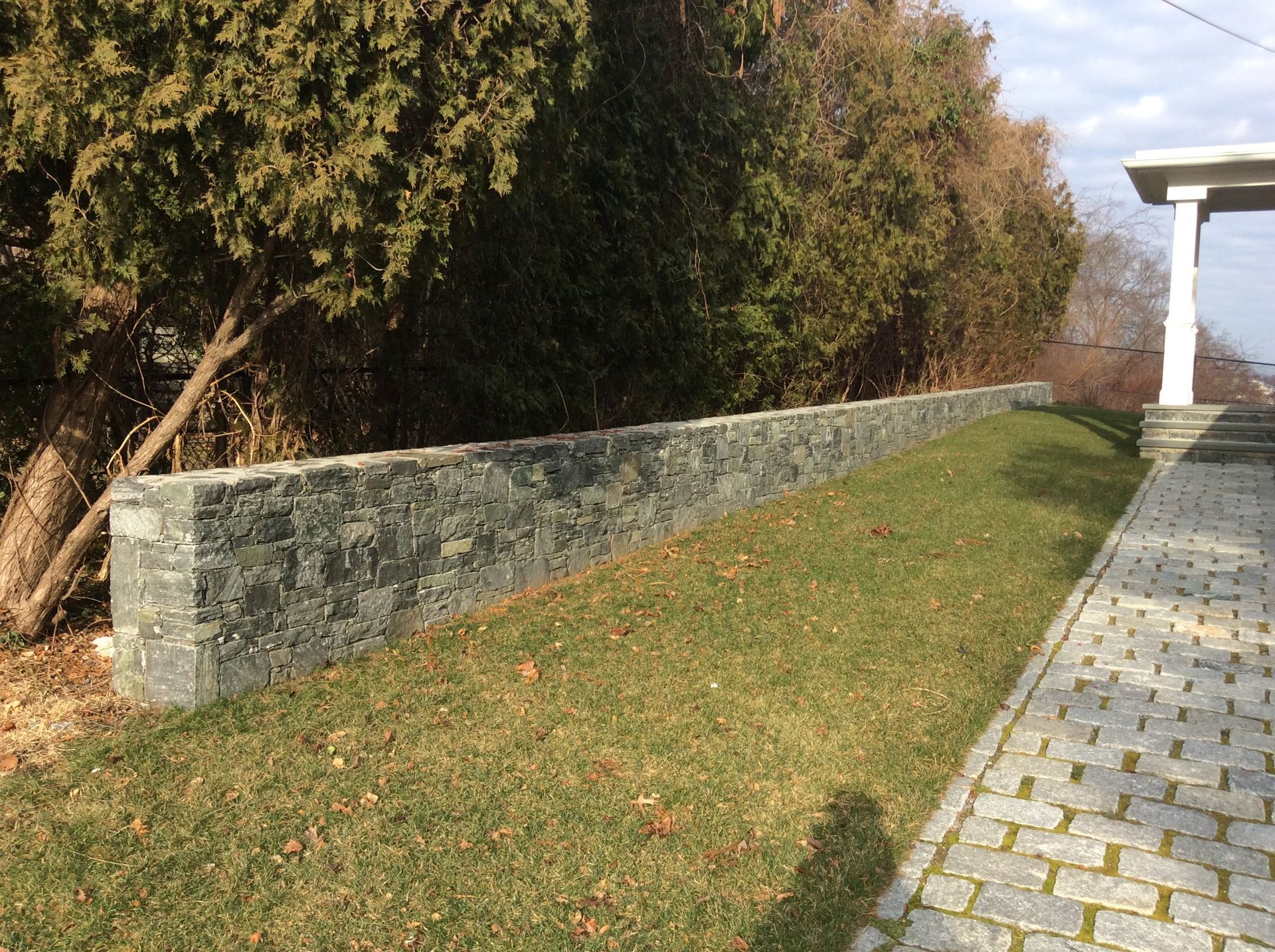 a stone wall is surrounded by grass and trees next to a brick walkway