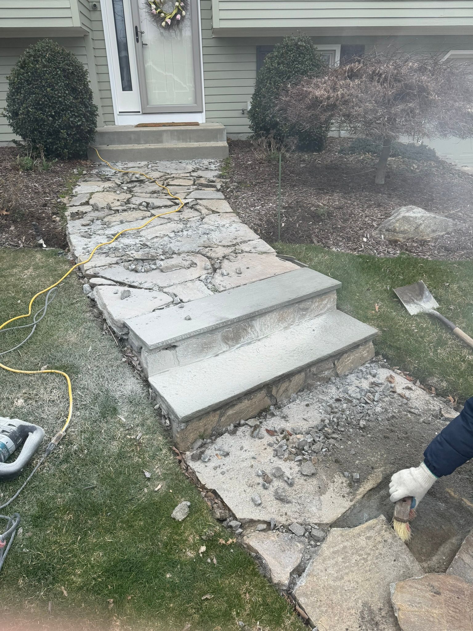 A person is working on a stone walkway in front of a house