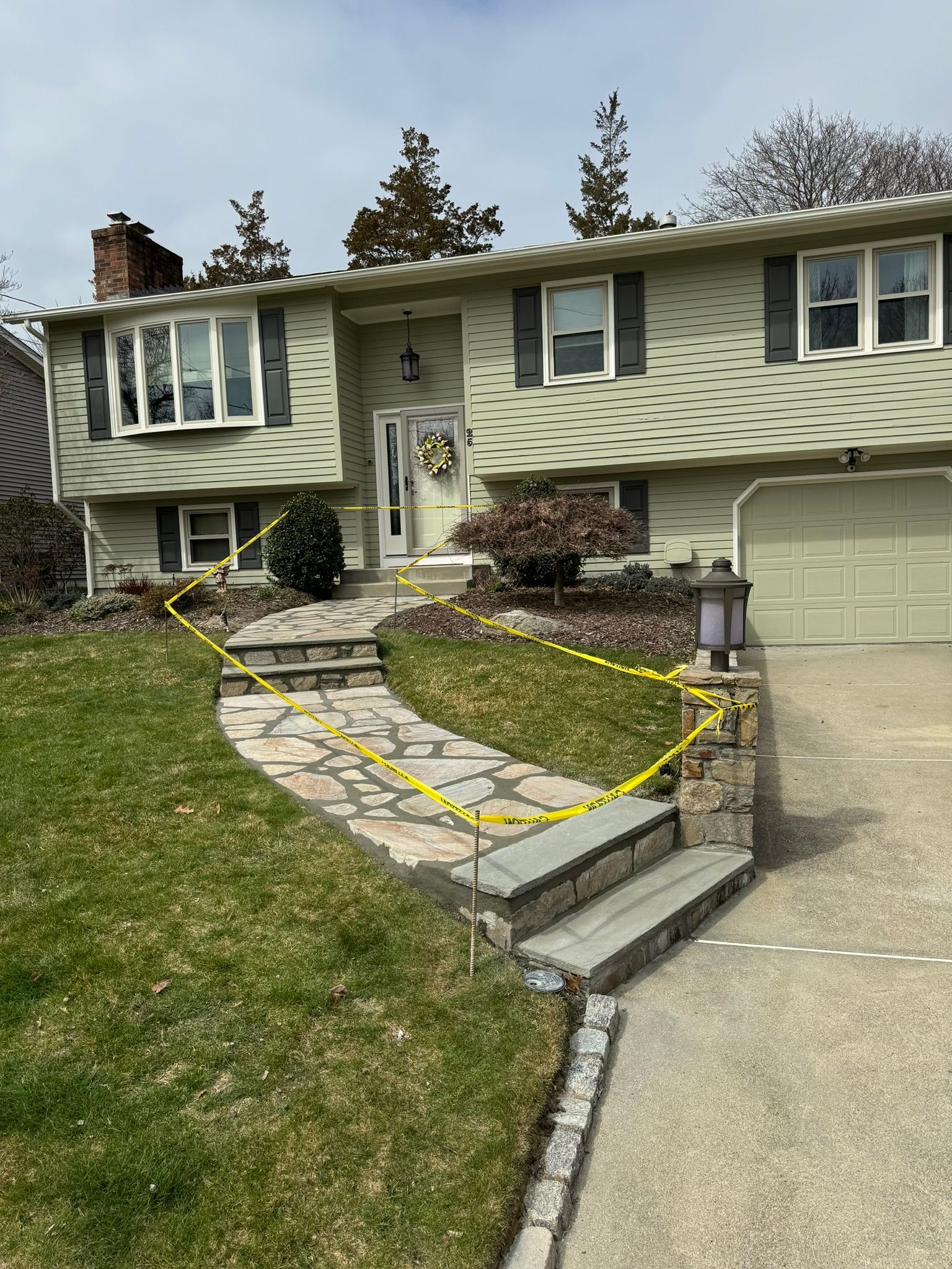 A house with a stone walkway leading to it is surrounded by yellow tape