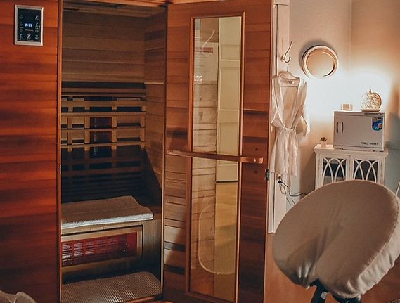 A wooden sauna with an open door, chair, robe, and towels in a spa-like room.