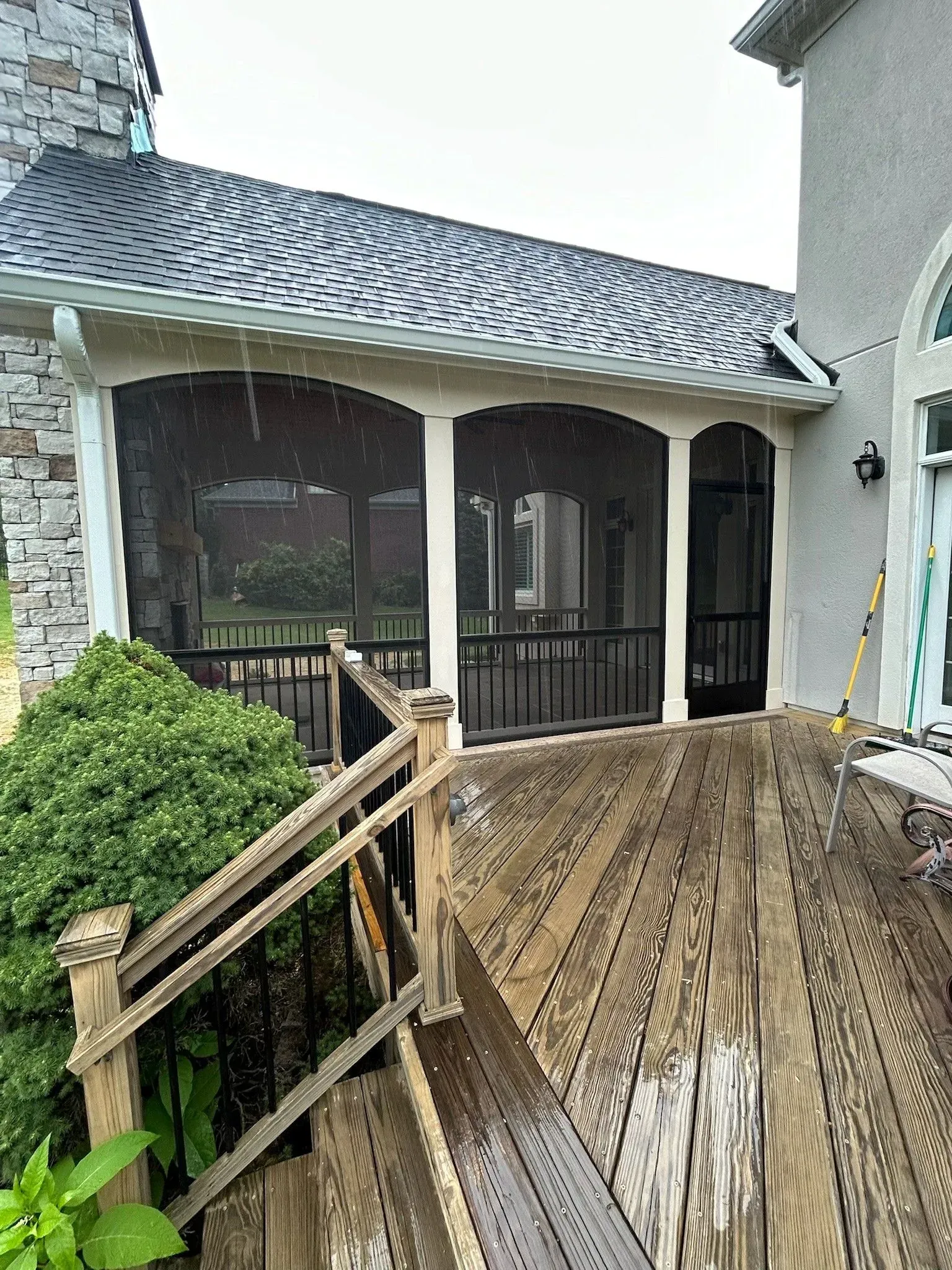 Wet wooden deck with screened porch, water droplets visible. Black railings, light-colored trim, and dark screens.