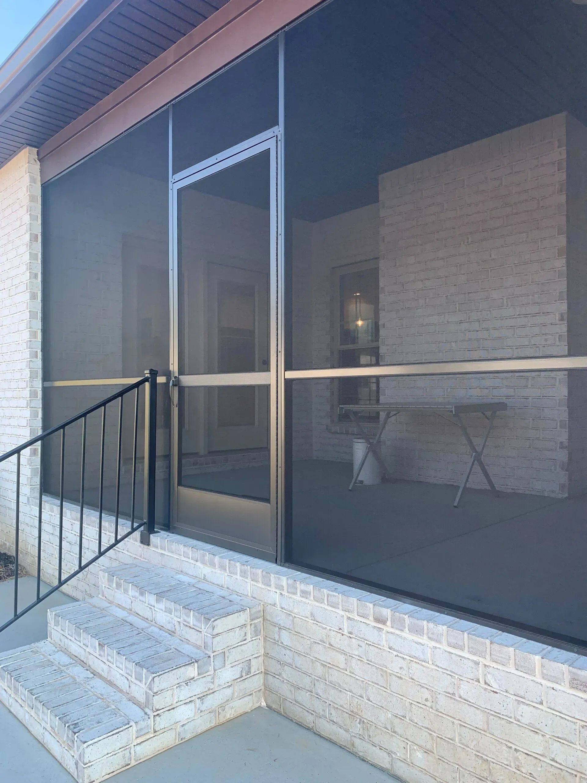 Screened porch with brick steps and walls, black railing. Metal-framed screen door.