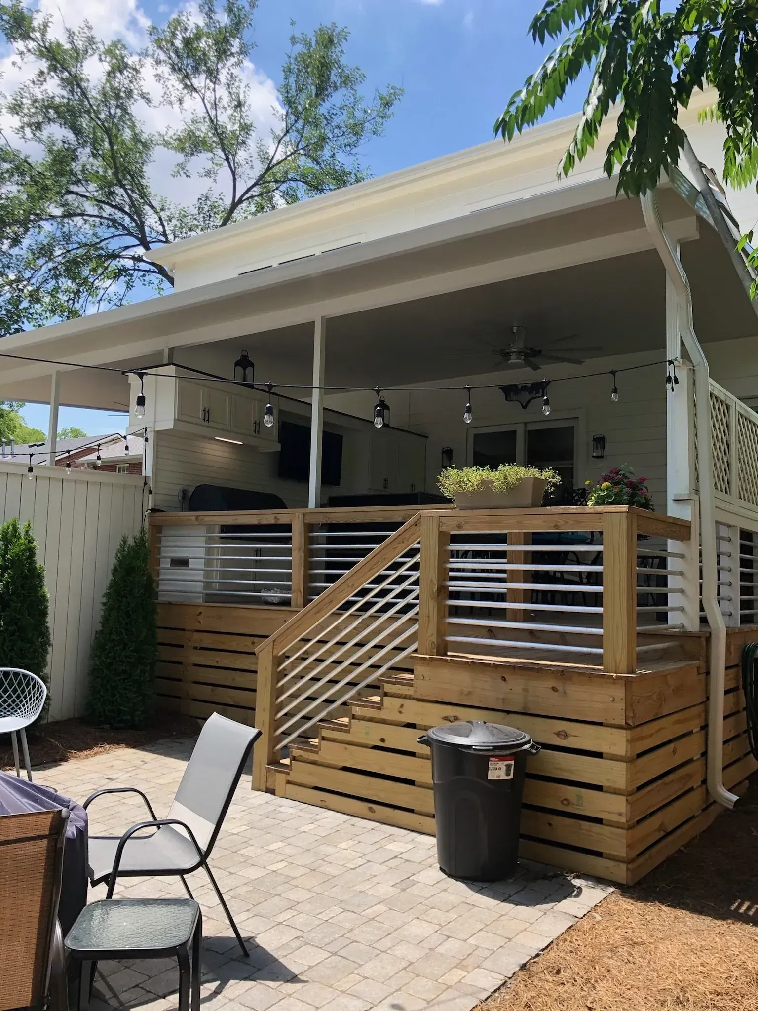 Wooden deck with railing, stairs, and overhead patio with lights and furniture.