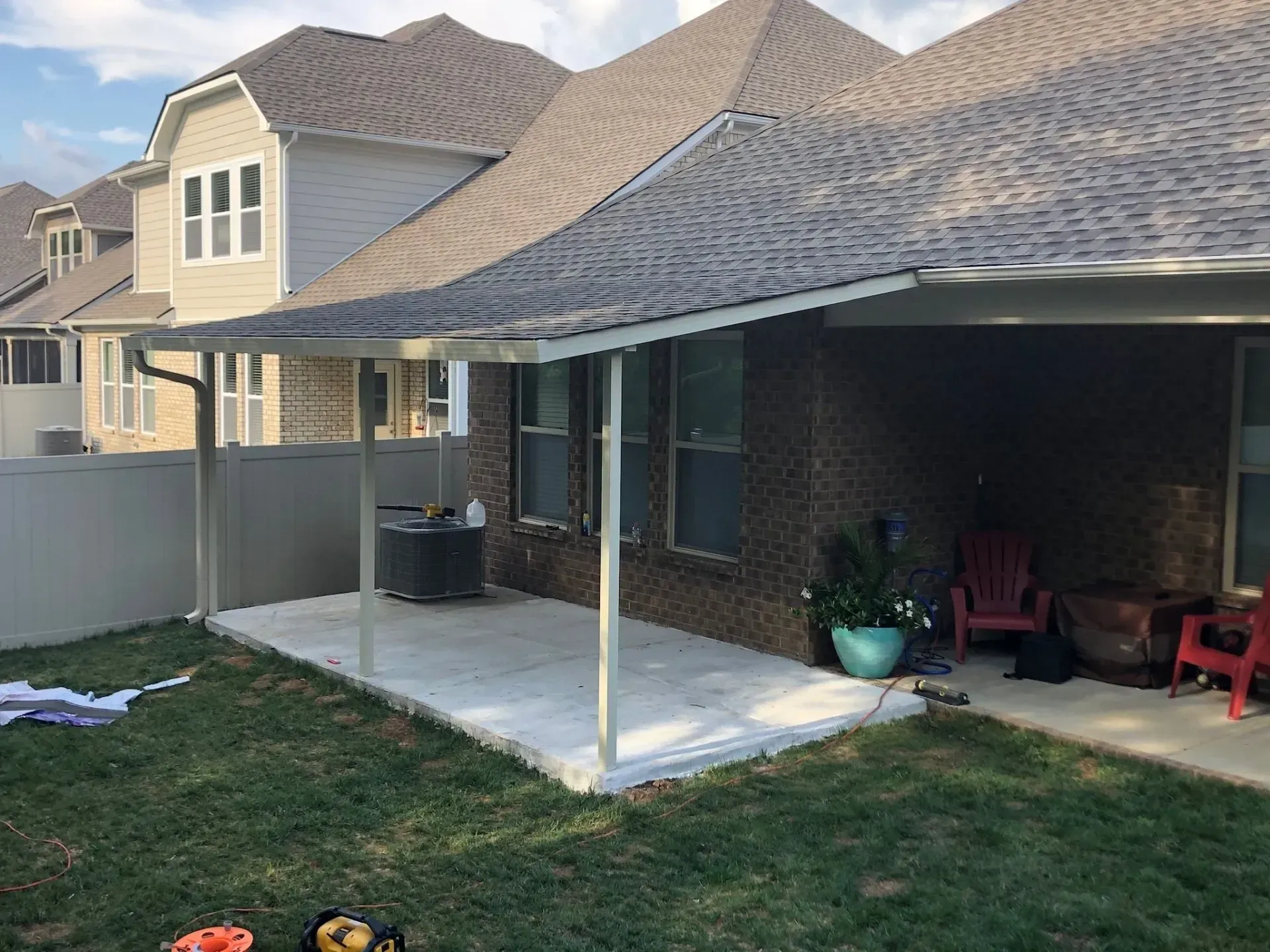 Patio with concrete slab, attached to a brick home with an overhanging roof. Green lawn in the foreground.