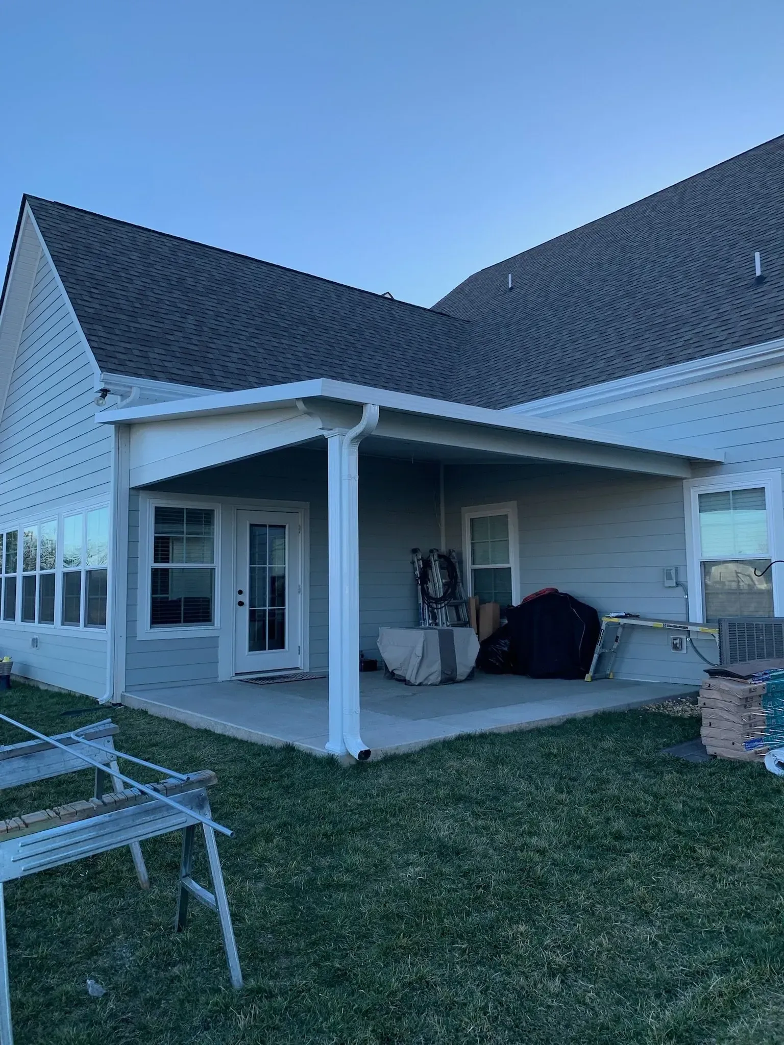 Backyard patio with a covered section, concrete flooring, and grass. The house has a gray roof and siding.