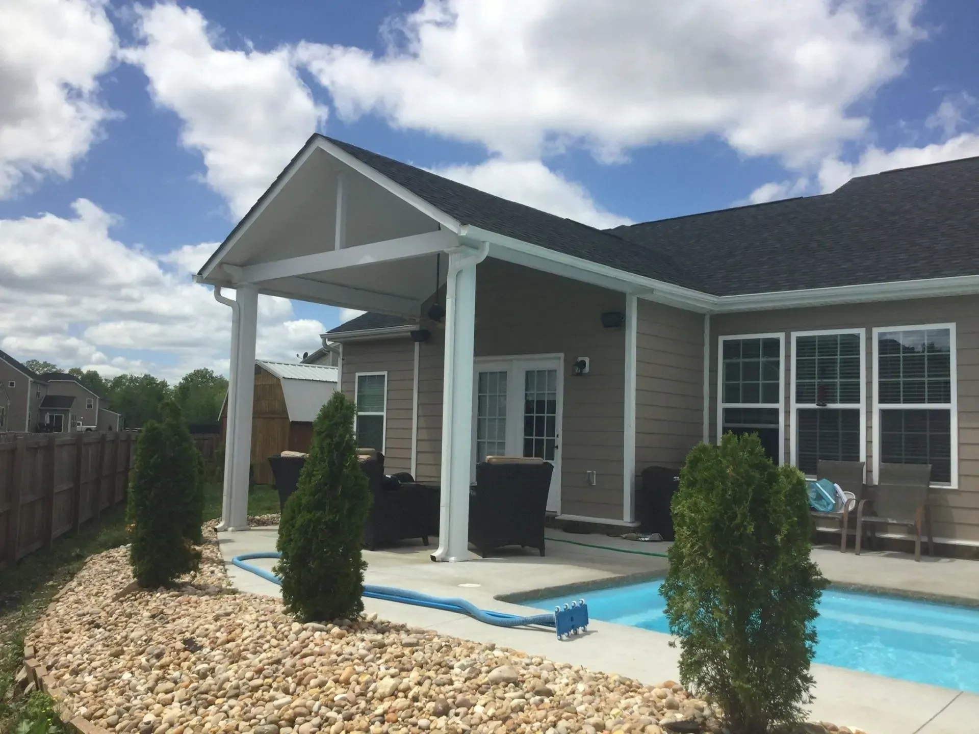 Backyard with pool, patio cover, tan house, and blue sky with clouds.