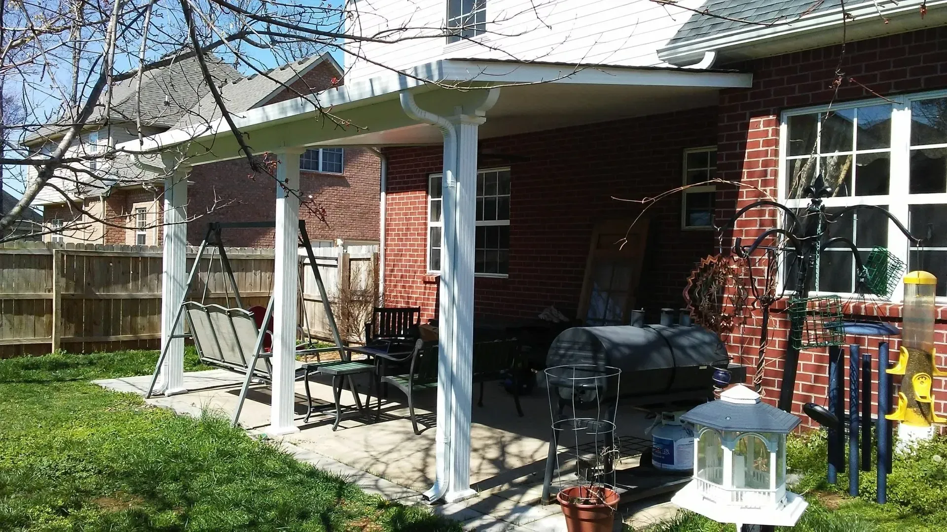 Patio with white columns and roof attached to brick house, outdoor furniture visible.