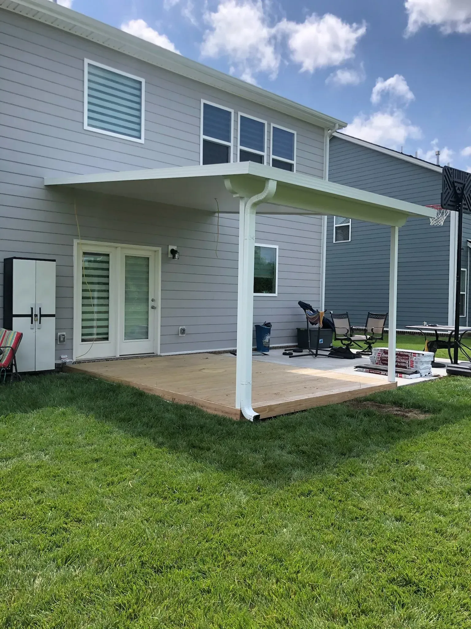 Backyard patio with white awning, gray house, and green grass.