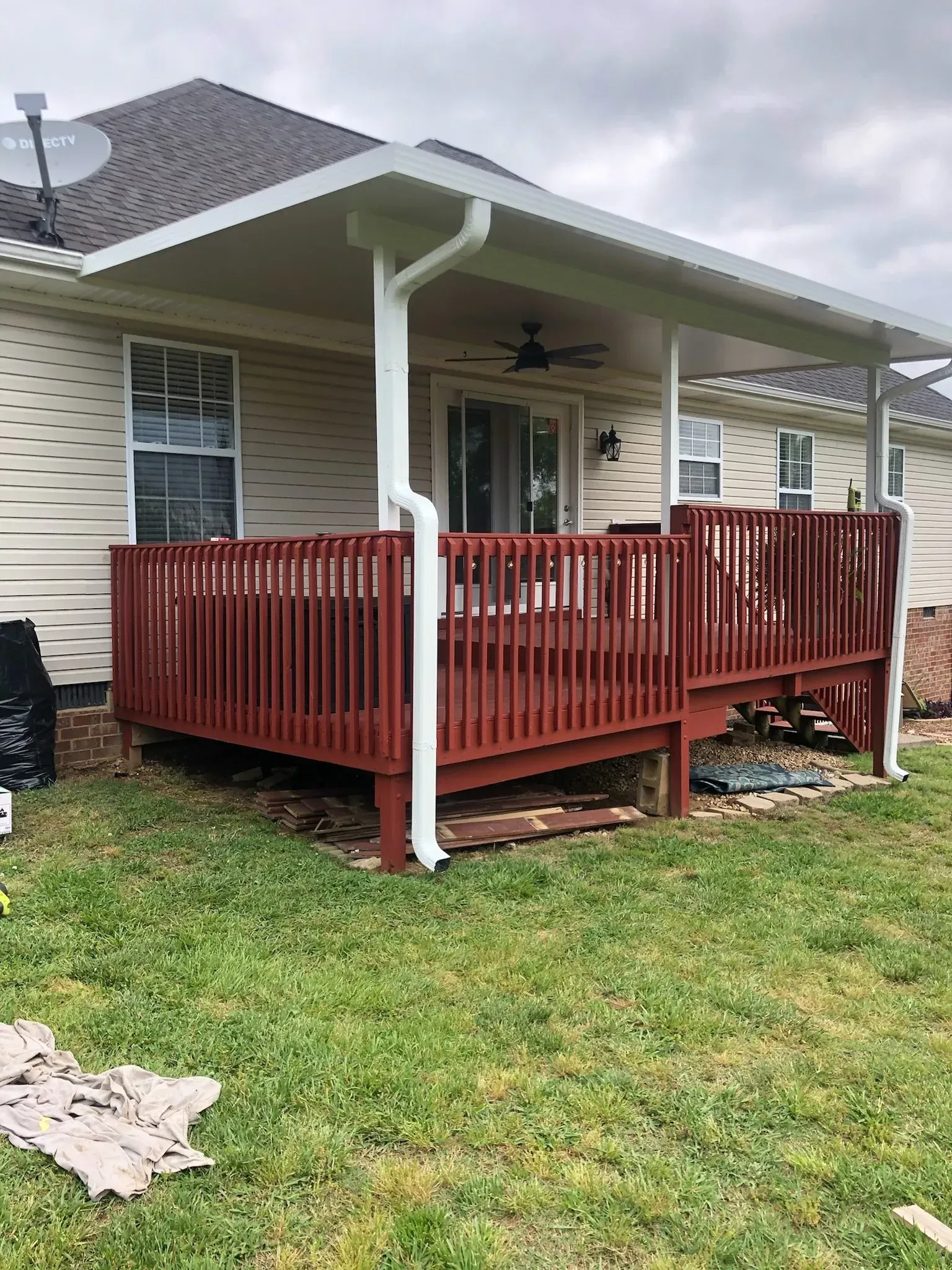 Red wooden deck with overhead roof attached to a beige house, white gutters, and a grassy yard.