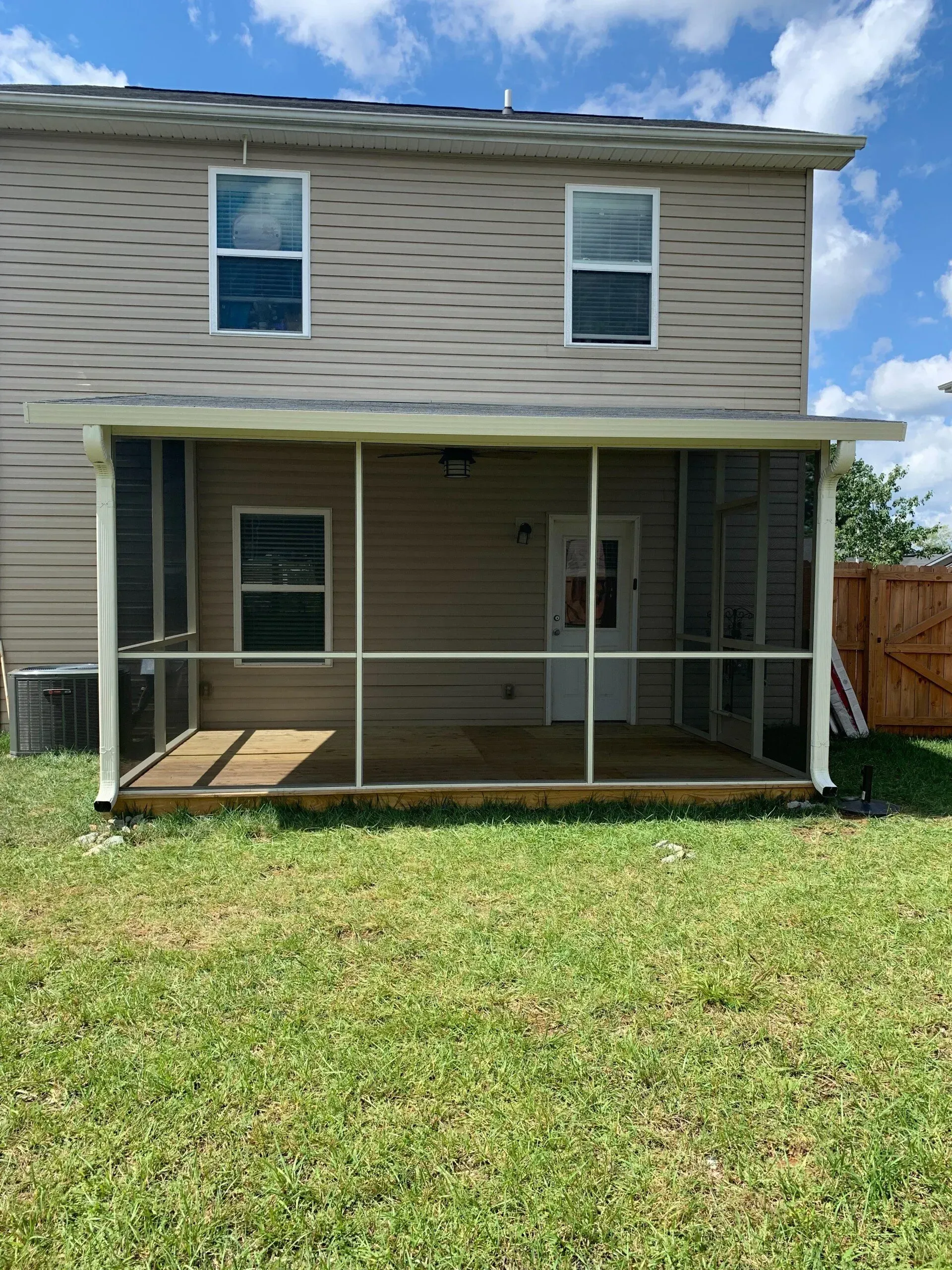 Screened porch attached to a two-story beige house with a wooden deck and green grass.