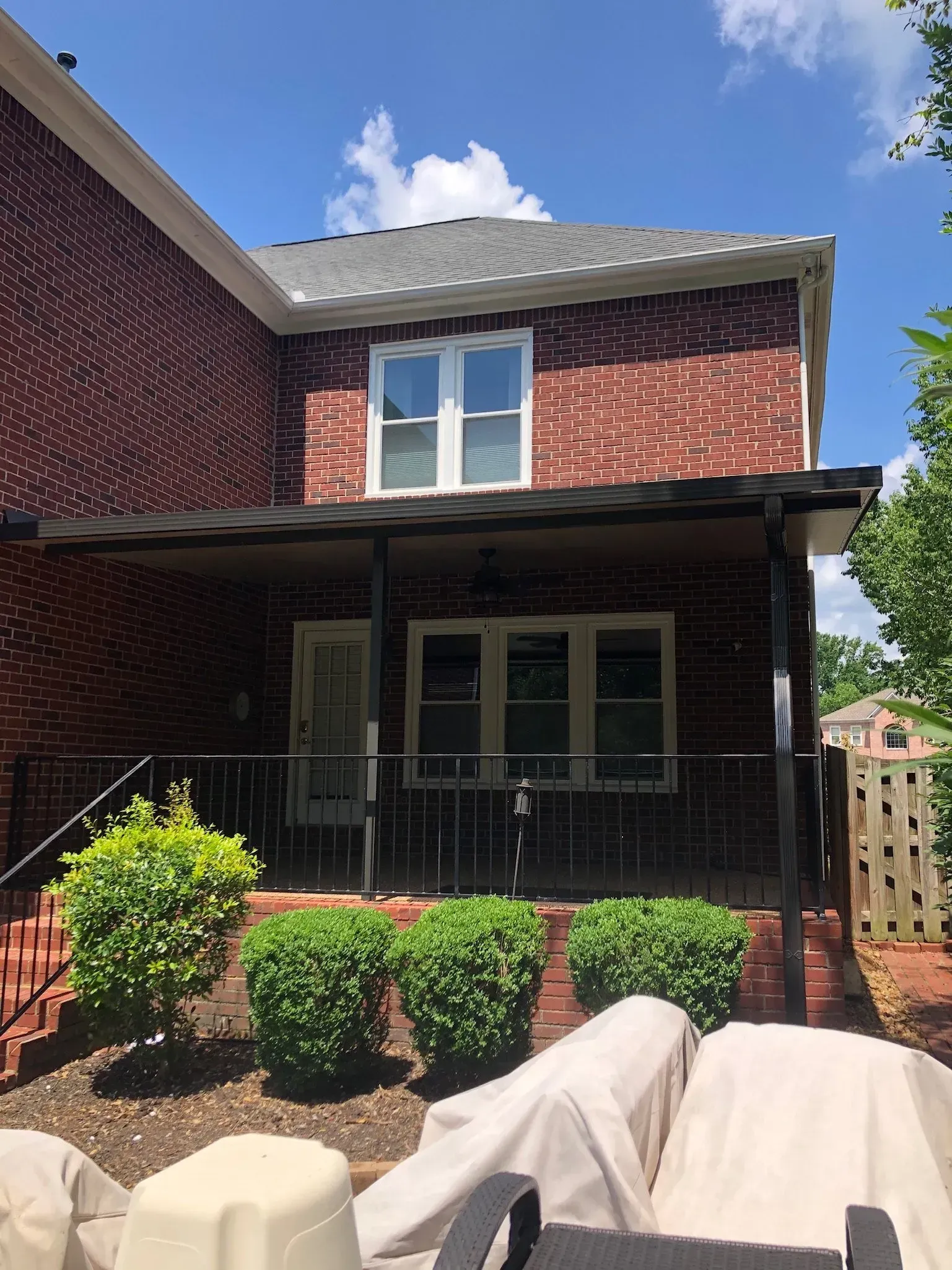 Brick house exterior with porch, windows, and bushes under a blue sky.