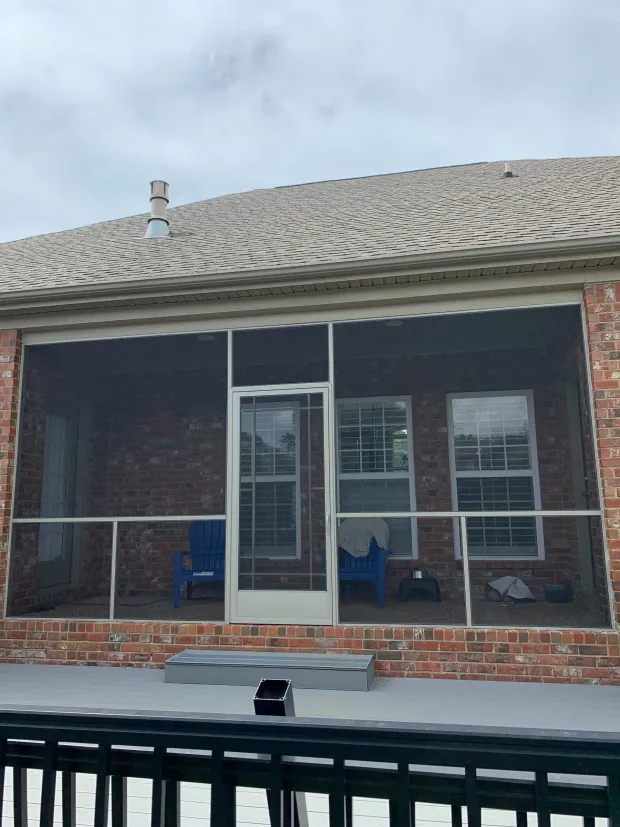 Screened porch with brick exterior, blue chairs, white door, and windows. Overcast sky.