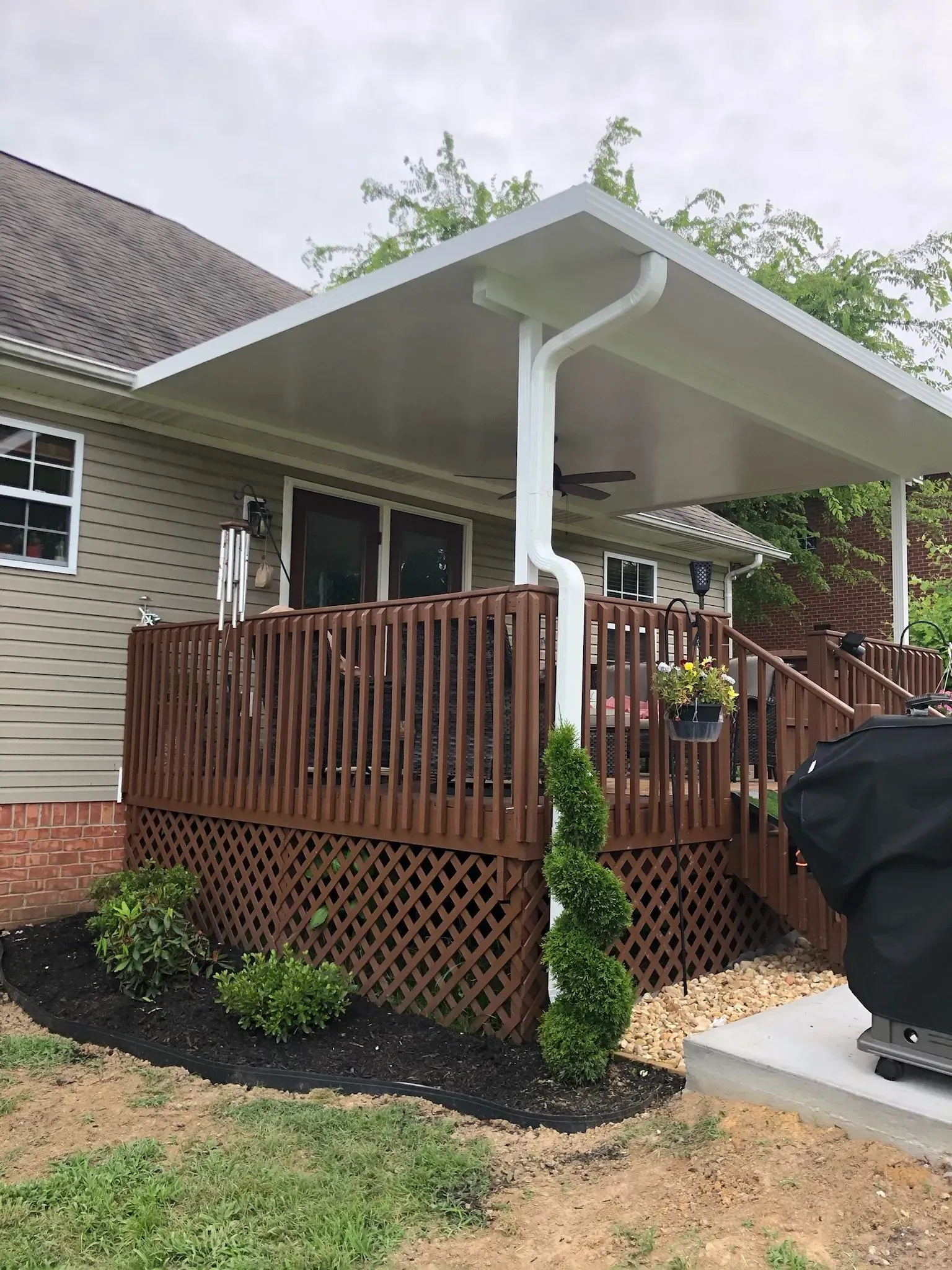 A deck with a white awning, brown railing, and latticework. A white downspout runs down a support beam.