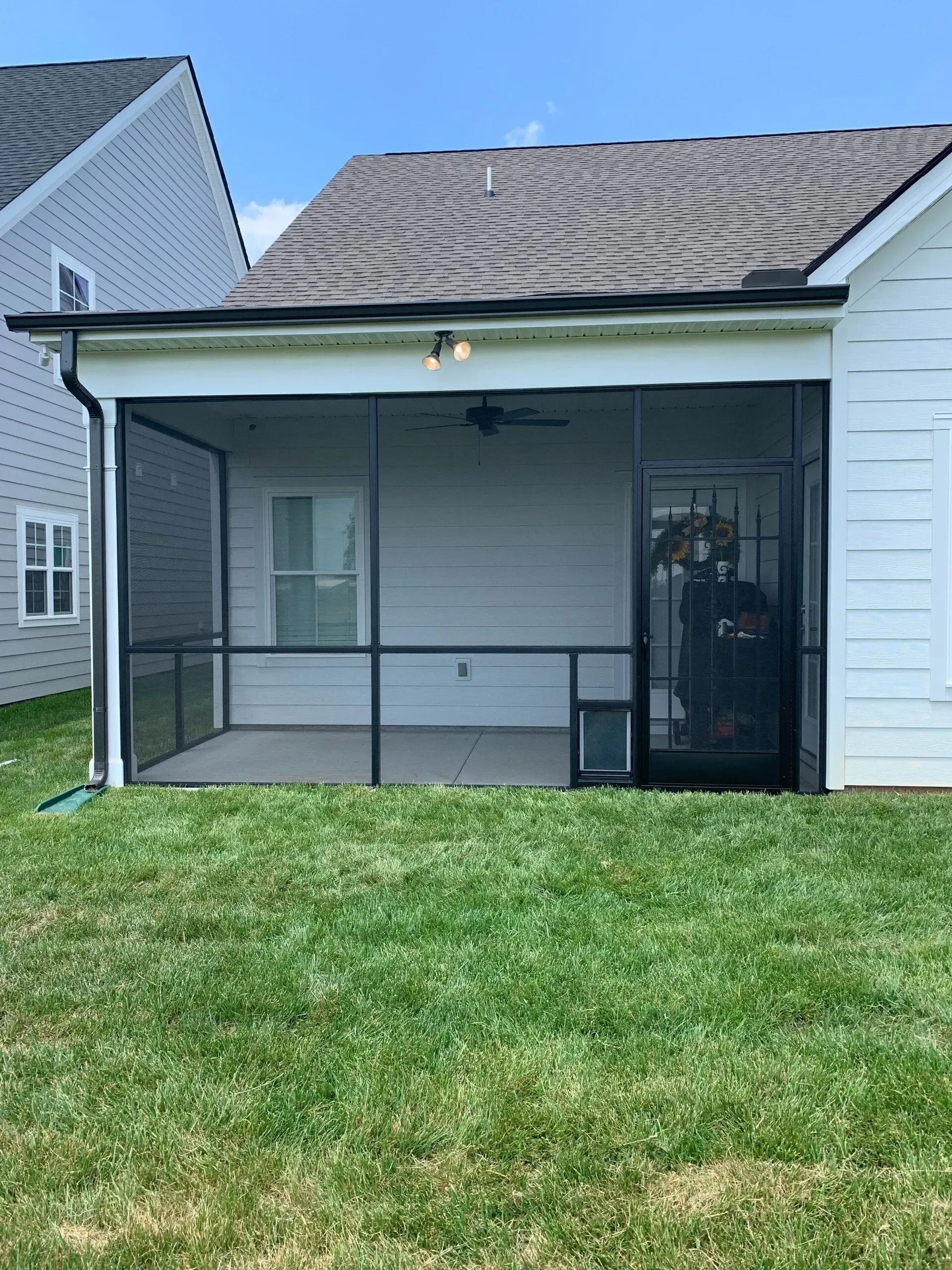 Screened-in porch on a house with dark screens, a door, and a pet door; green grass in the yard.