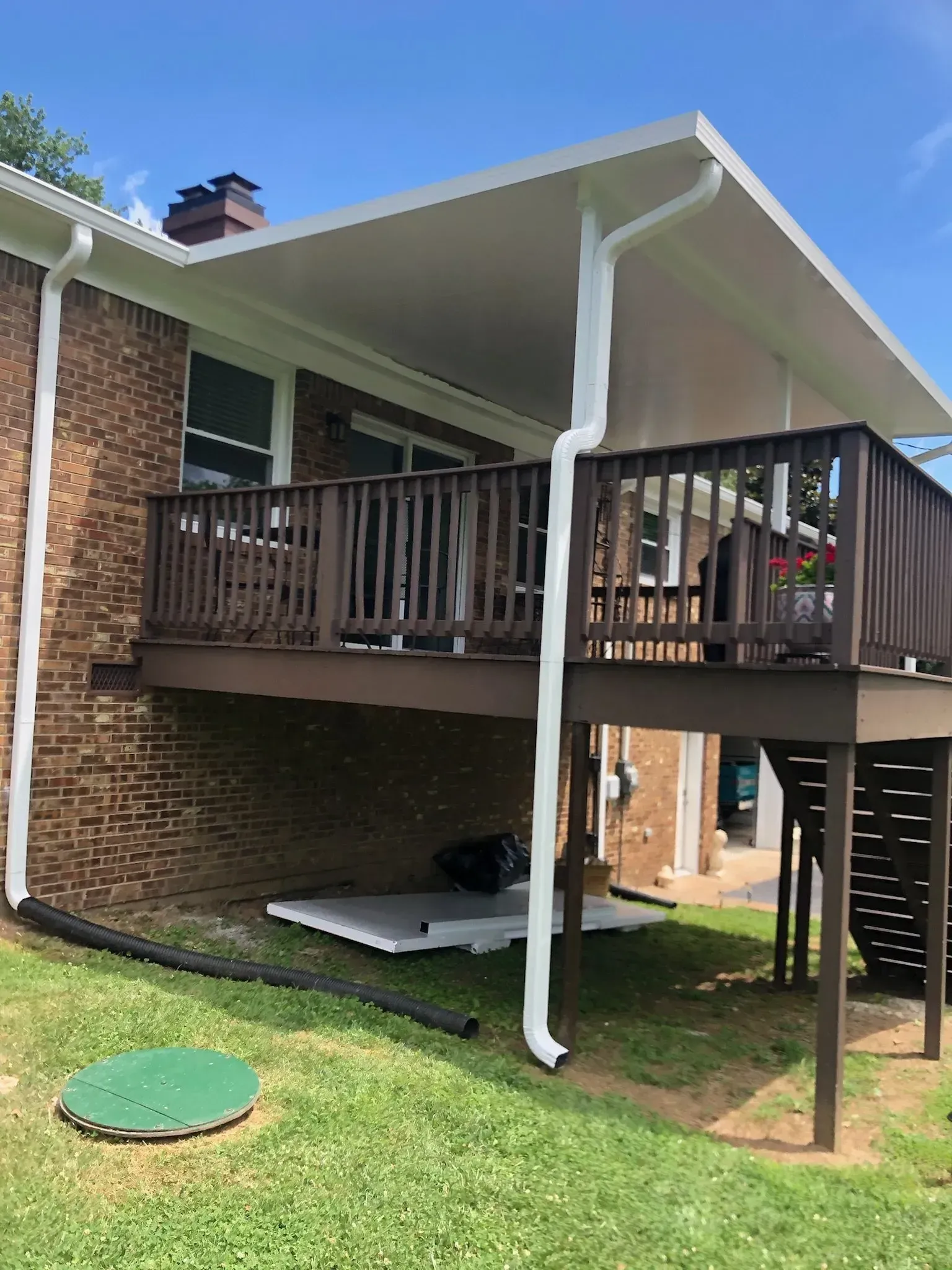 Brick house with a covered wooden deck. White gutters, green grass, and blue sky.