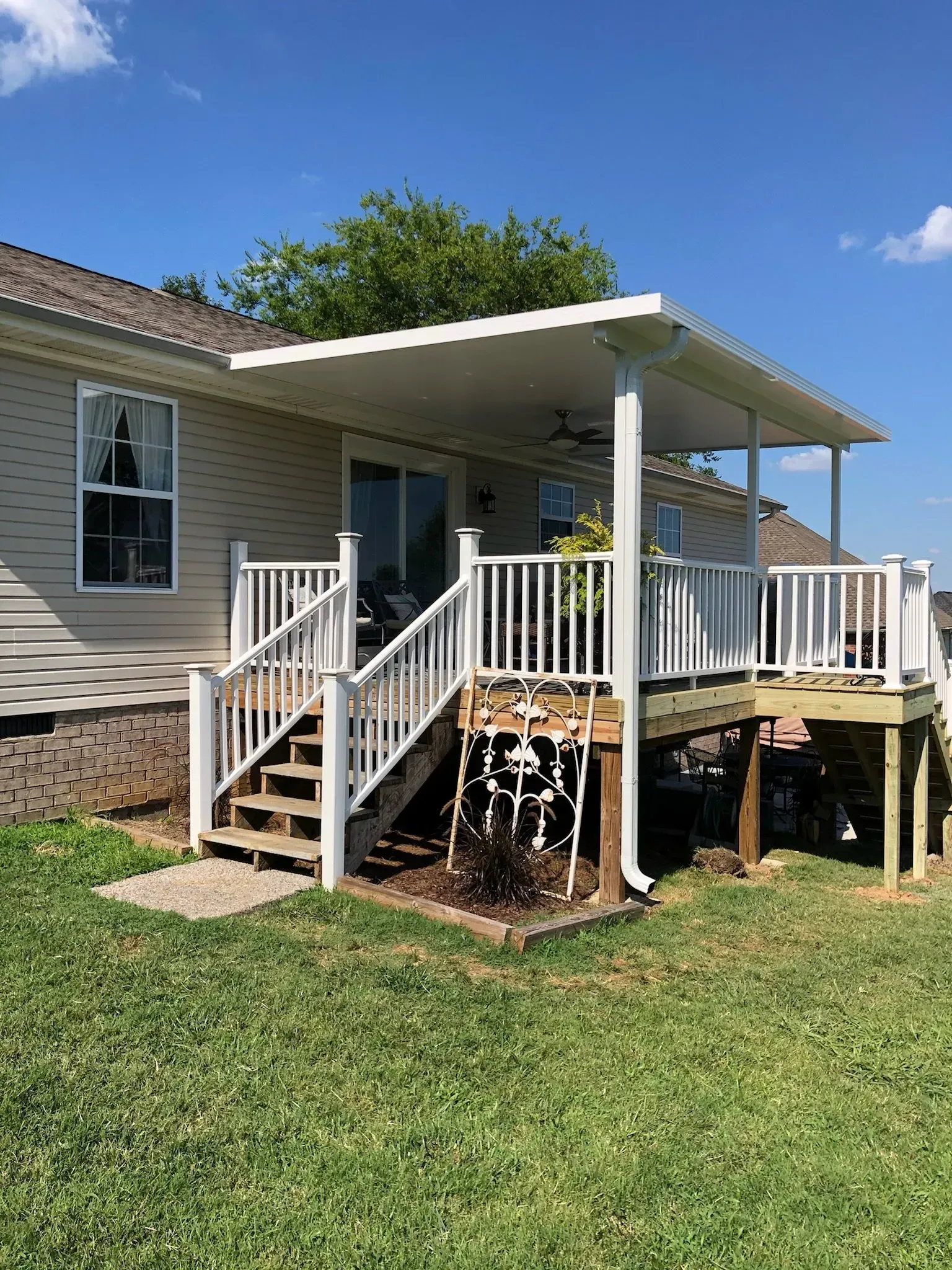 Backyard deck with white railing, covered by a white awning; sunny, blue sky.