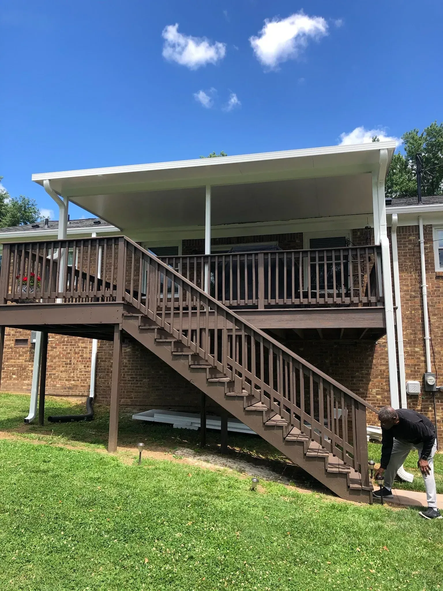 Wooden deck with stairs, covered by a white awning. A person stands on the ground near the stairs.