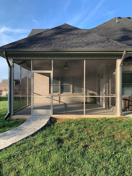 Screened porch attached to a brick house with a concrete walkway and green grass under a blue sky.