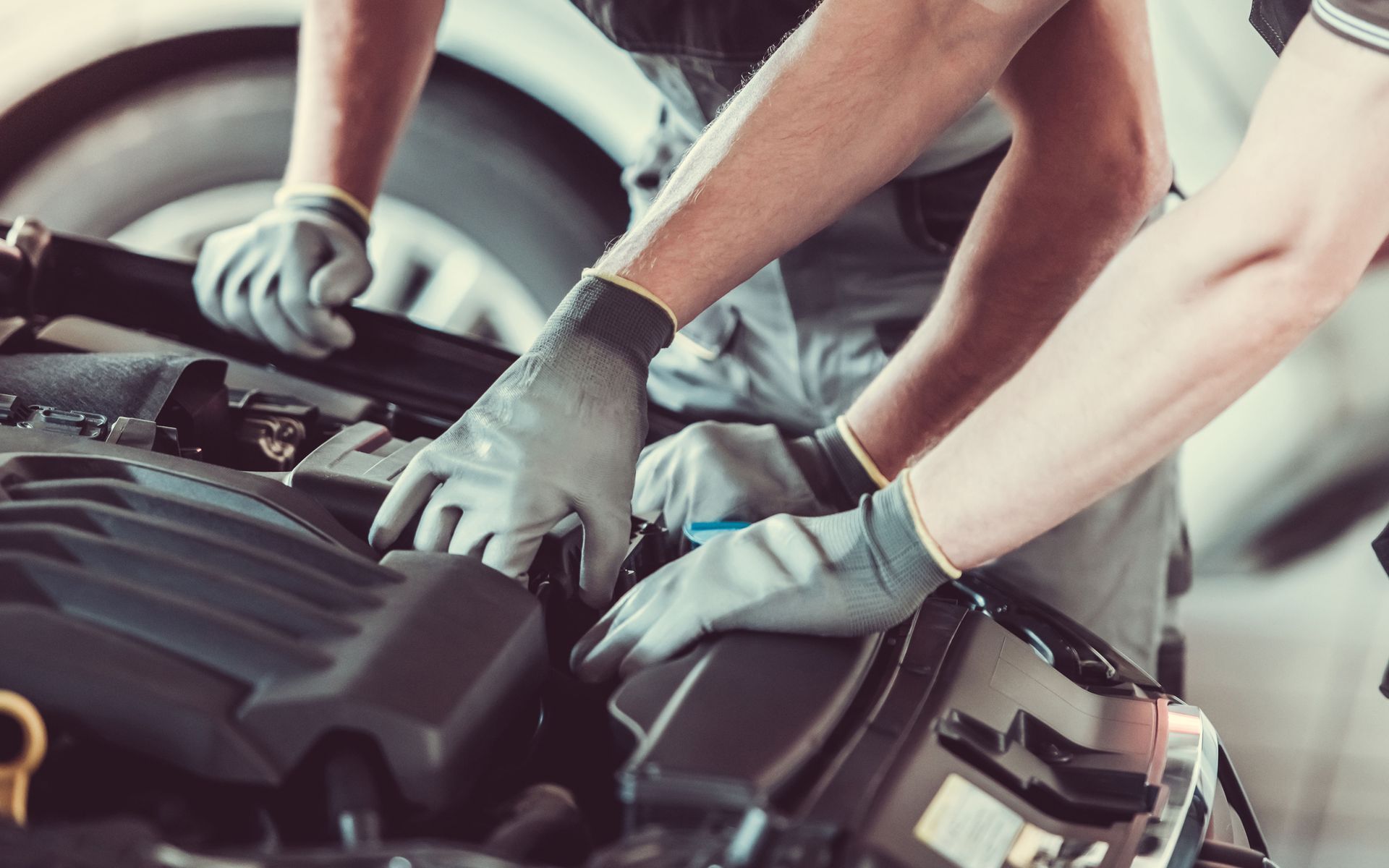 Mechanics in gray gloves work on a car engine in a garage.
