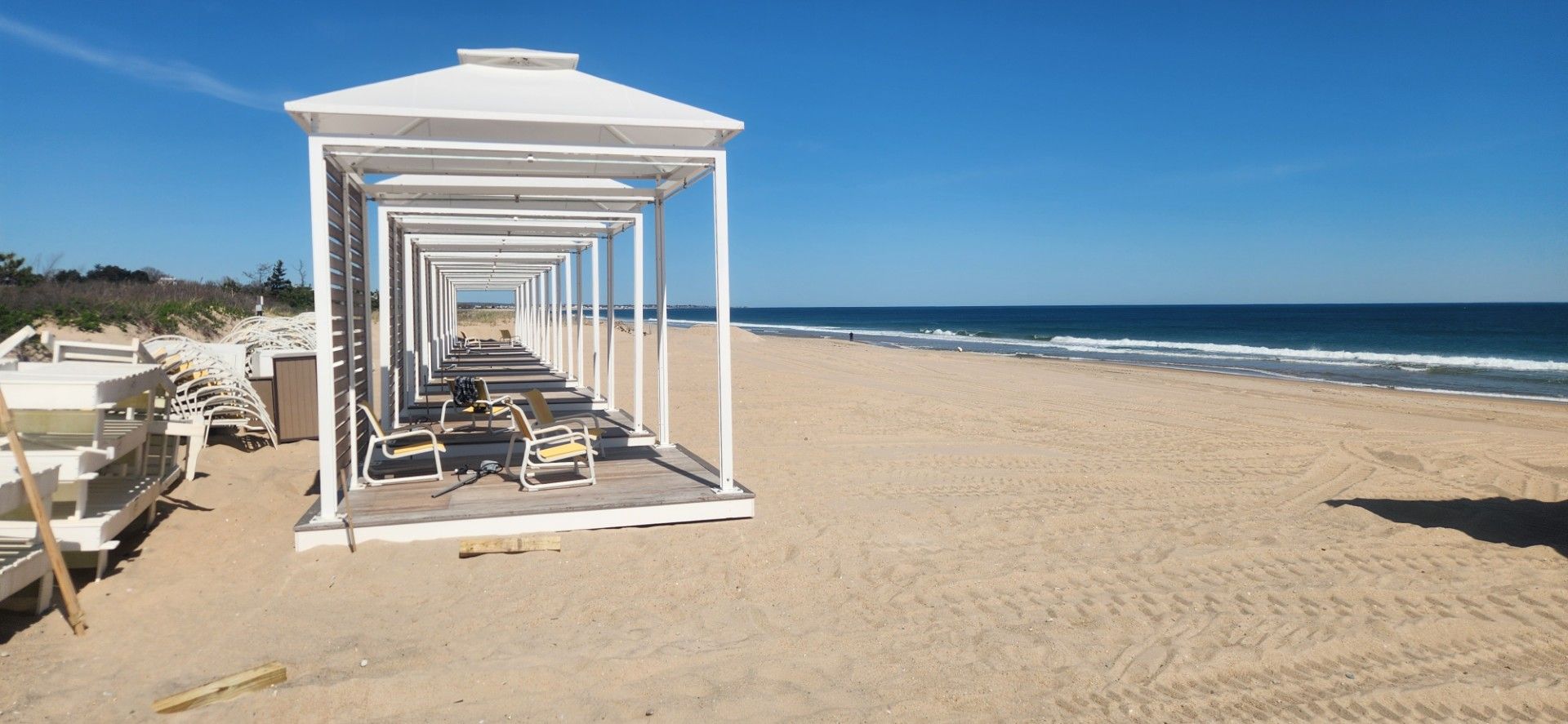 White-framed structures on a sandy beach, leading toward the ocean under a clear blue sky.
