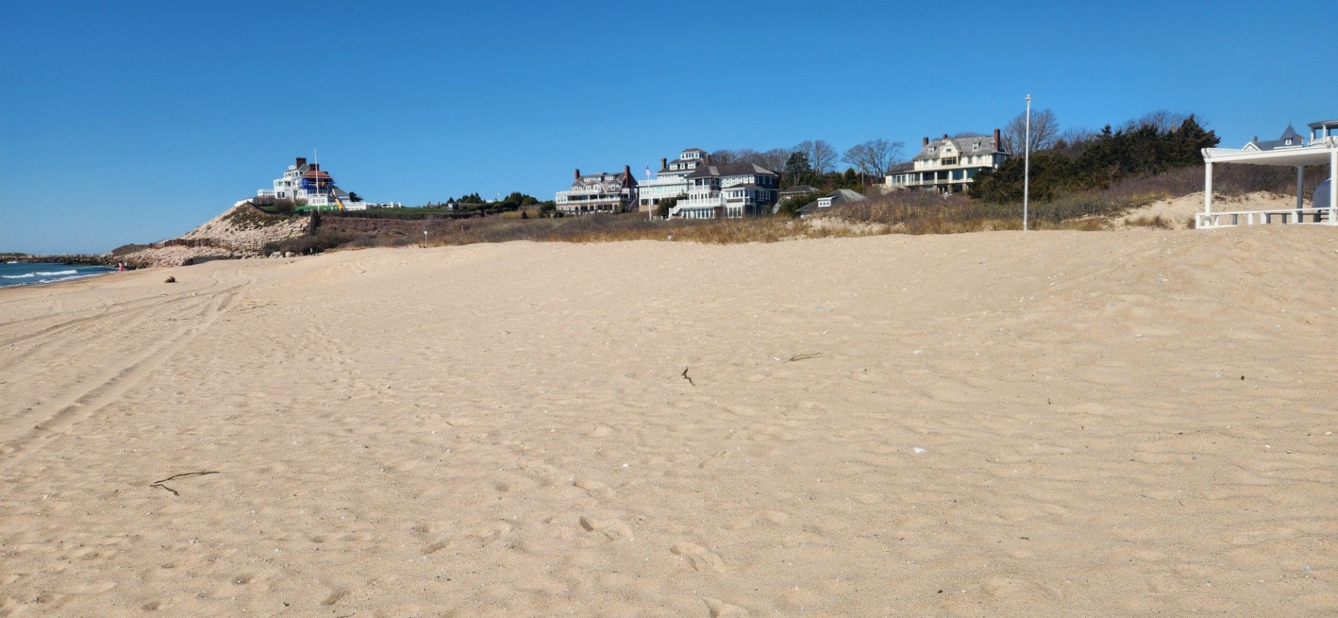 Beach scene with sandy shore, blue sky, and houses along the coast.
