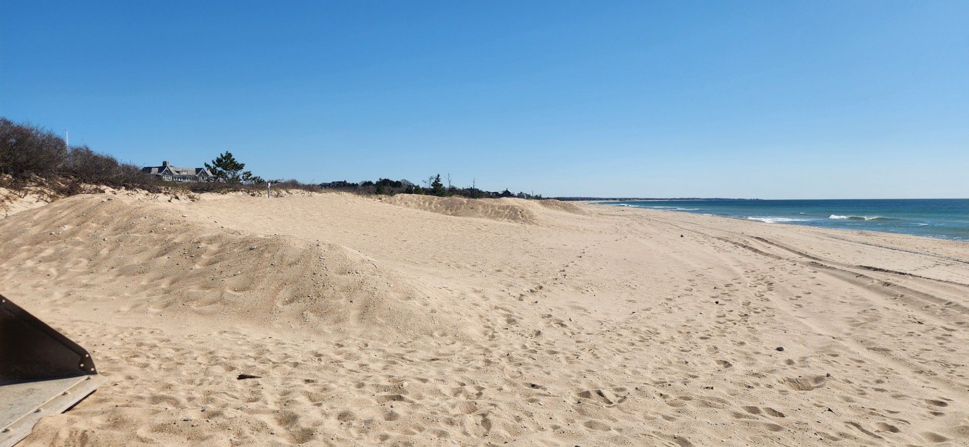 Sandy beach under a clear blue sky. Ocean waves gently roll in.