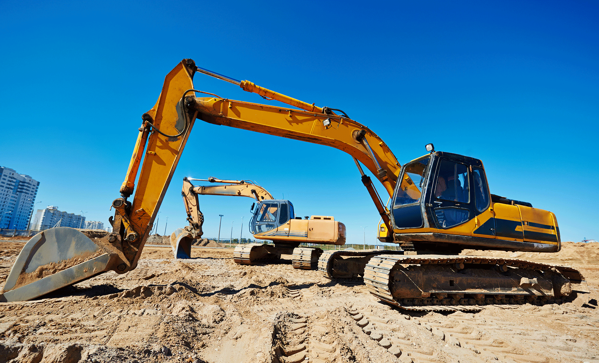 Two yellow excavators are working on a construction site.