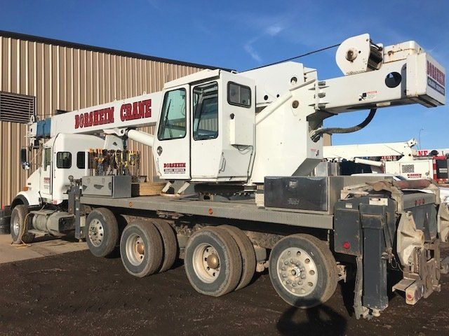A white truck with a crane on the back is parked in front of a building