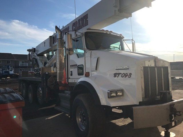 A white truck with a crane attached to it is parked in a parking lot.